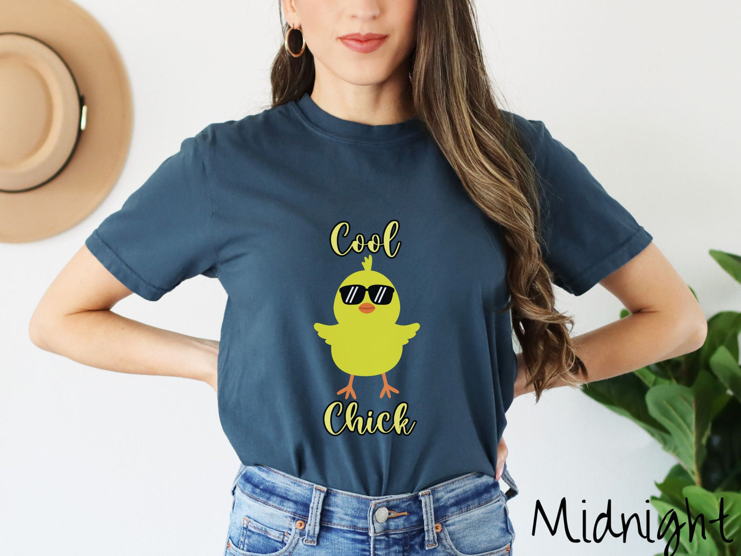 A woman wearing a cute, vintage midnight colored shirt with the yellow text Cool Chick and below is a yellow baby chick with black sunglasses with its wings spread. It has an orange mouth and feet and yellow feathers sticking out the top of its head.
