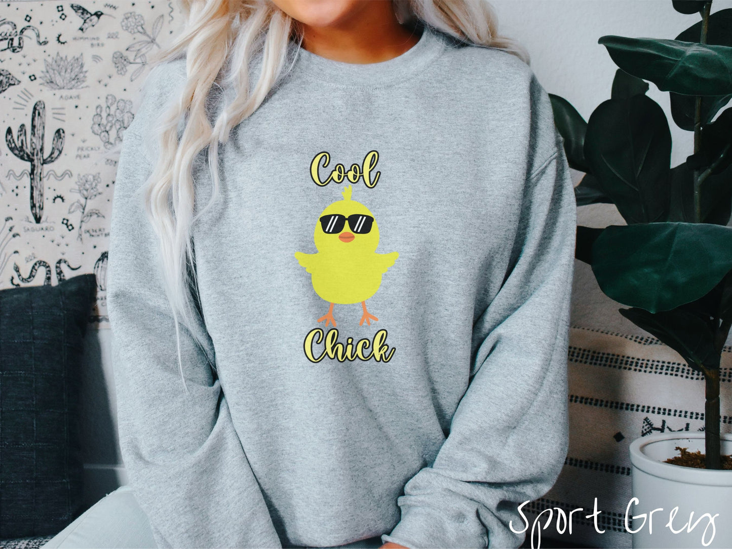 A woman wearing a cute, vintage sport grey colored sweatshirt with yellow text Cool Chick and below is a yellow baby chick with black sunglasses with its wings spread. It has an orange mouth and feet and yellow feathers sticking out of its head.