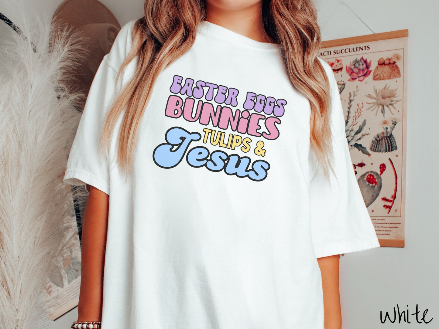 A woman wearing a cute, vintage white colored shirt with text Easter Eggs, Bunnies, Tulips, & Jesus in purple, pink, yellow, and blue font.