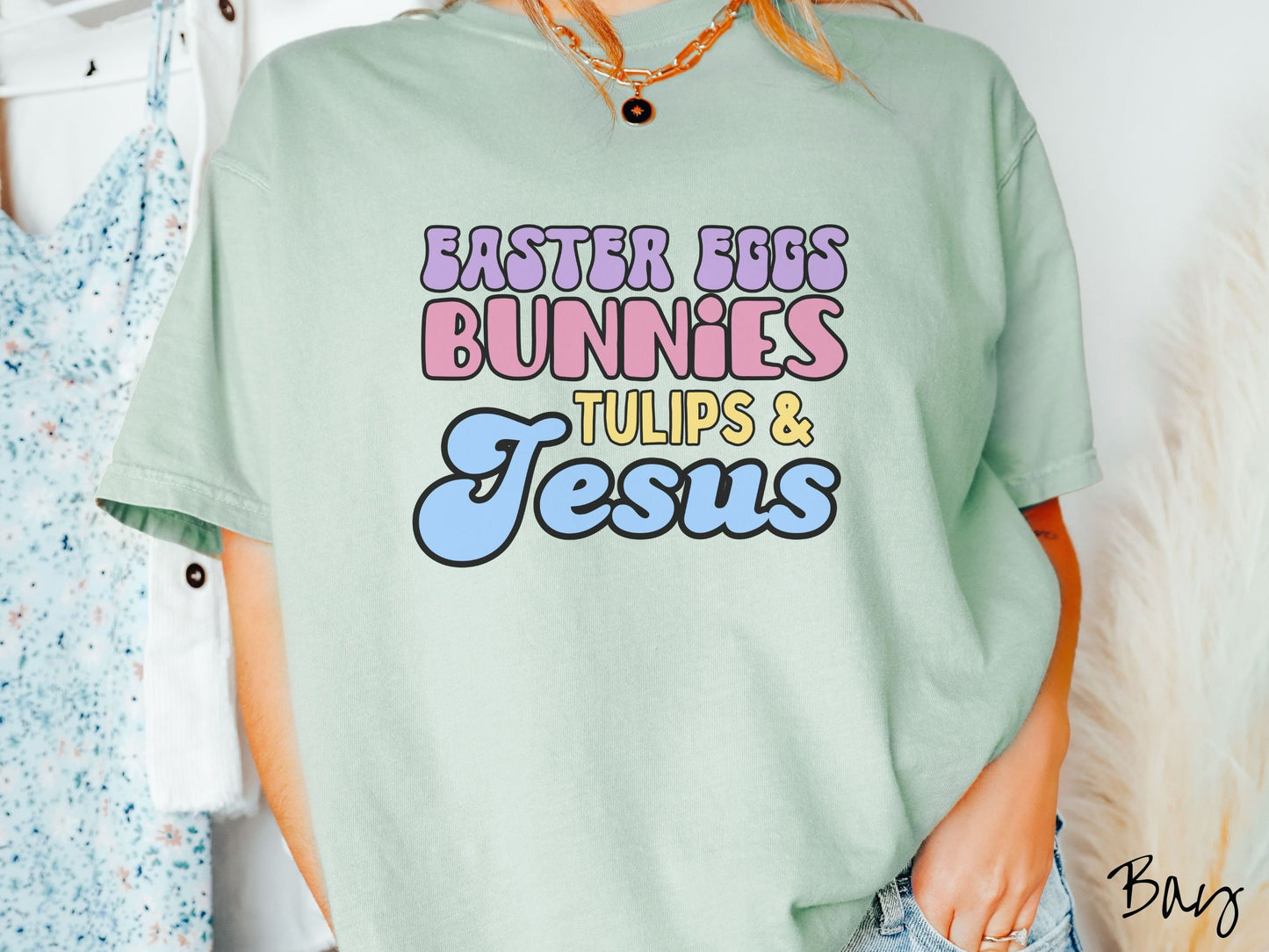 A woman wearing a cute, vintage bay colored shirt with text Easter Eggs, Bunnies, Tulips, & Jesus in purple, pink, yellow, and blue font.