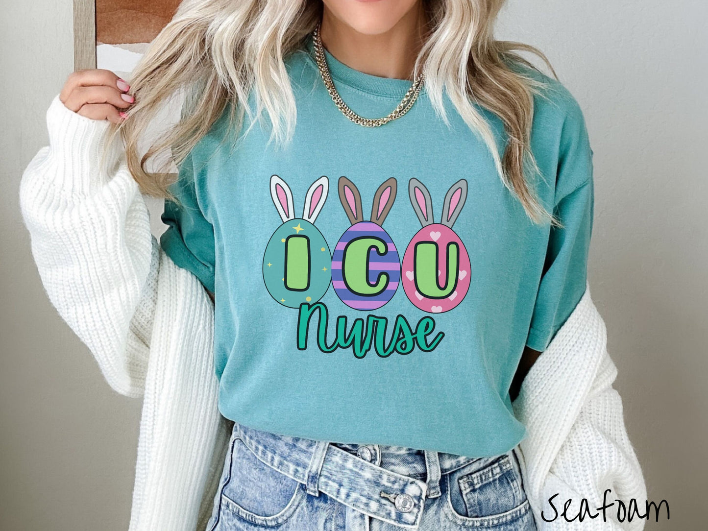 A woman wearing a cute, vintage seafoam colored shirt with three colorful easter eggs next to each other with the letters I, C, and U inside. Each egg has a pair of bunny rabbit ears, one is white, the middle brown, and the left gray.