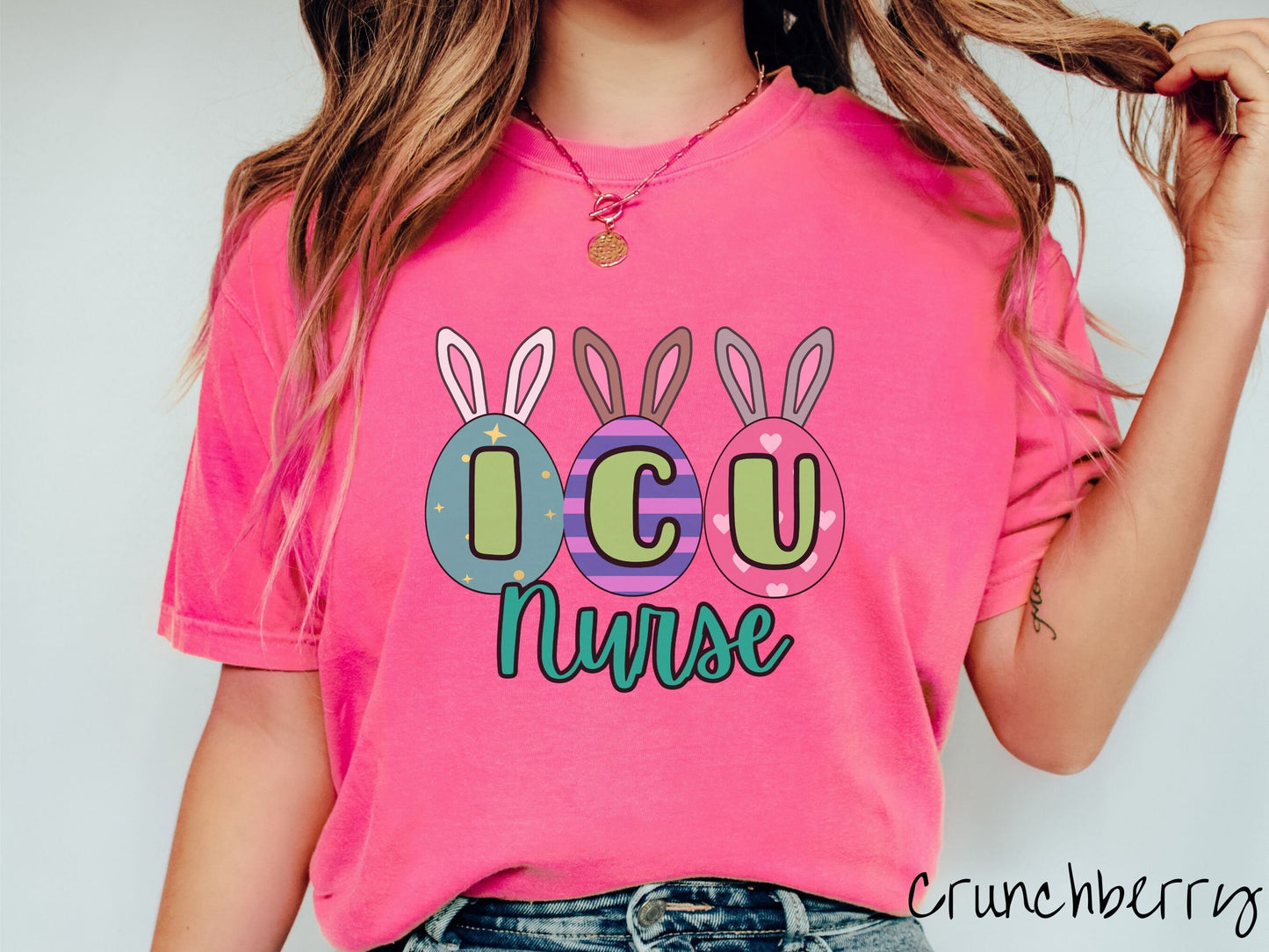 A woman wearing a cute, vintage crunchberry colored shirt with three colorful easter eggs next to each other with the letters I, C, and U inside. Each egg has a pair of bunny rabbit ears, one is white, the middle brown, and the left gray.