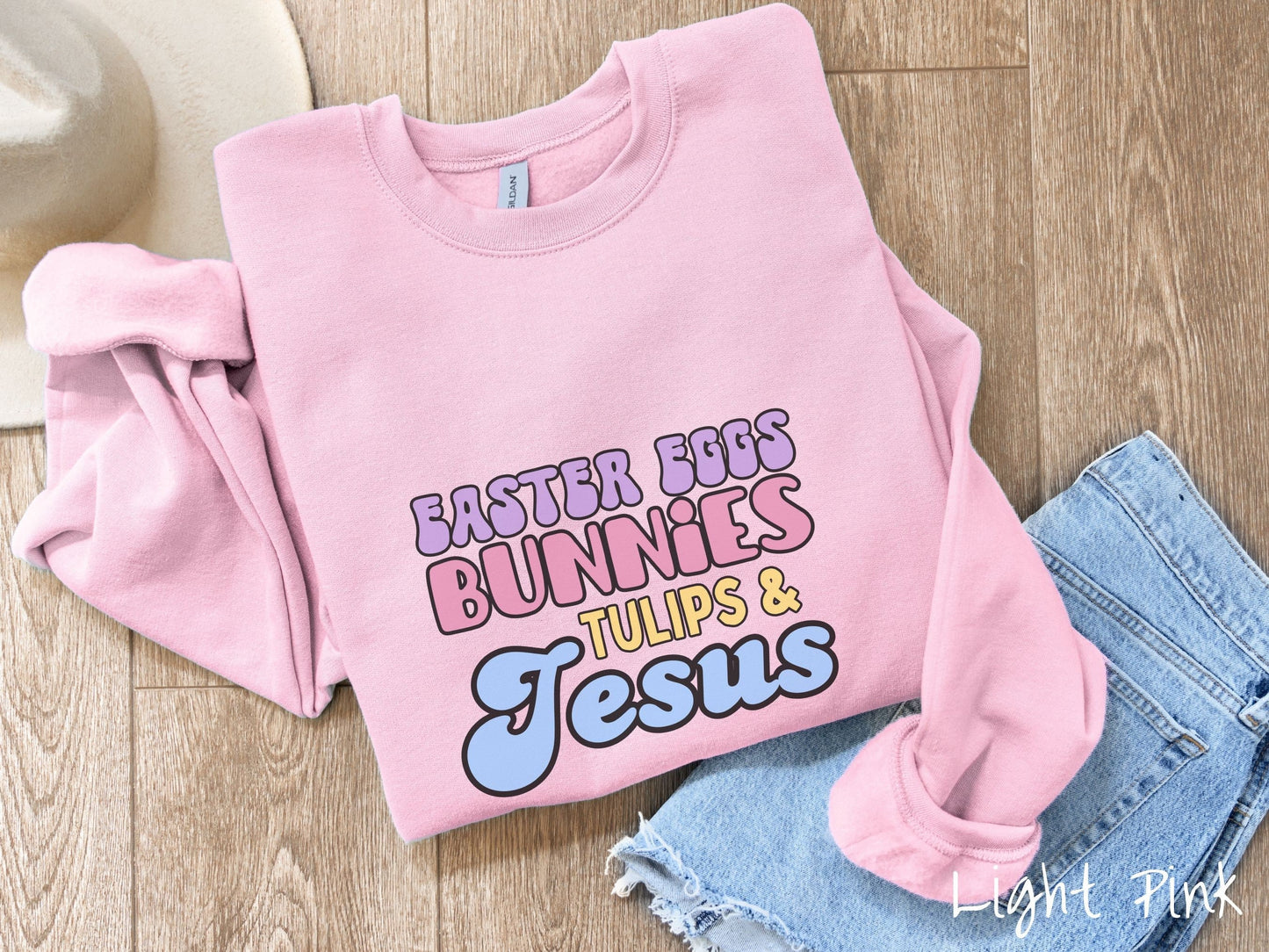 A cute, vintage light pink colored sweatshirt with text Easter Eggs, Bunnies, Tulips, & Jesus in purple, pink, yellow, and blue font.