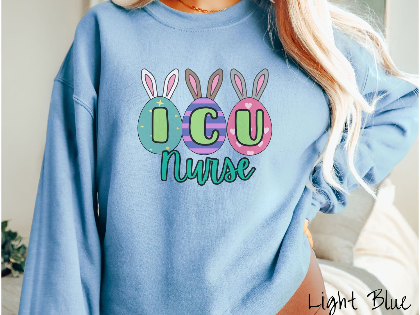 A woman wearing a cute, vintage light blue colored sweatshirt with three colorful easter eggs next to each other with the letters I, C, and U inside. Each egg has a pair of bunny rabbit ears, one is white, the middle brown, and the left gray.