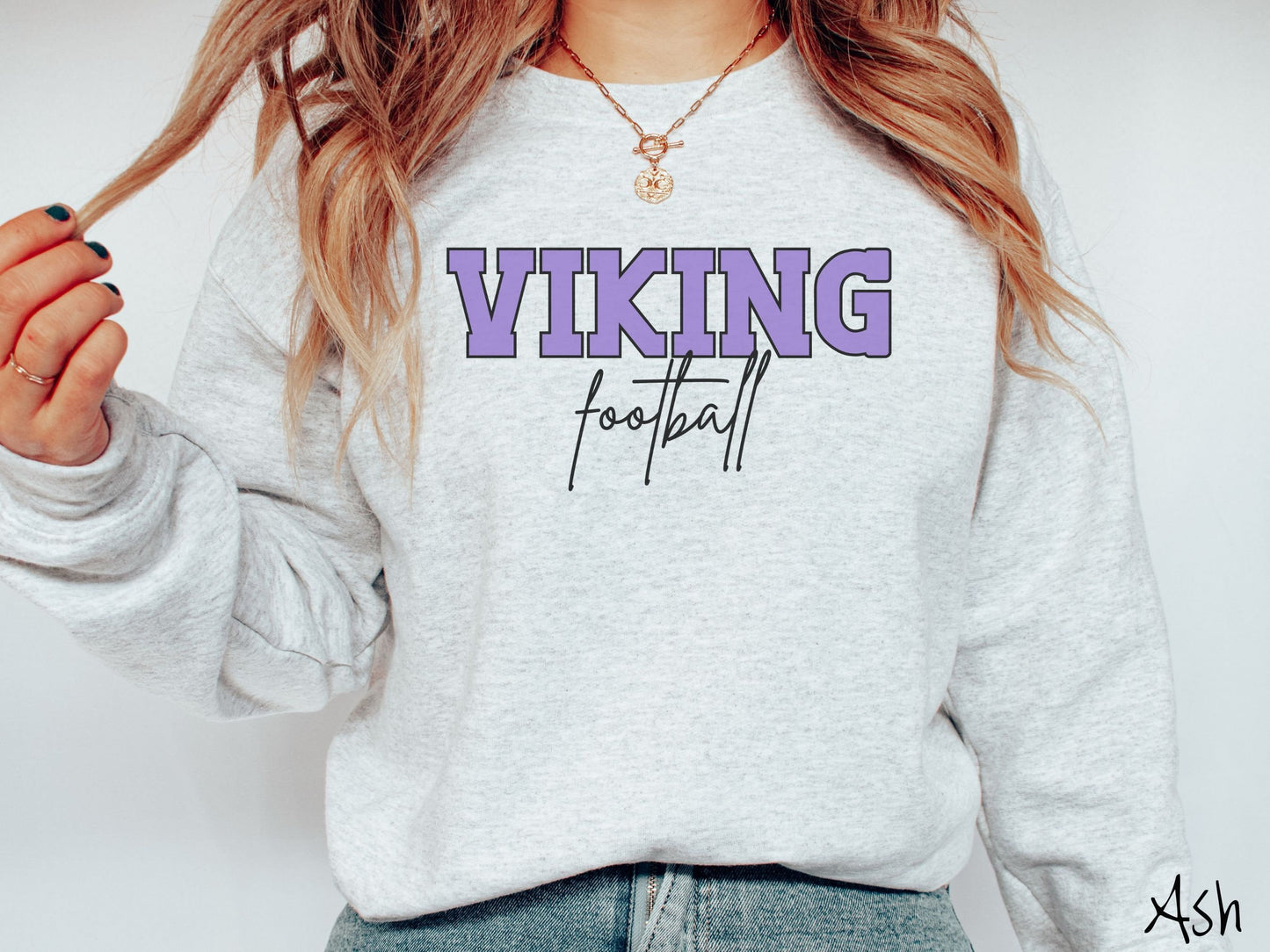 A woman wearing a cute, vintage ash colored sweatshirt with the word Viking in uppercase, purple font across the front and the word football below that in black, undercase cursive writing.