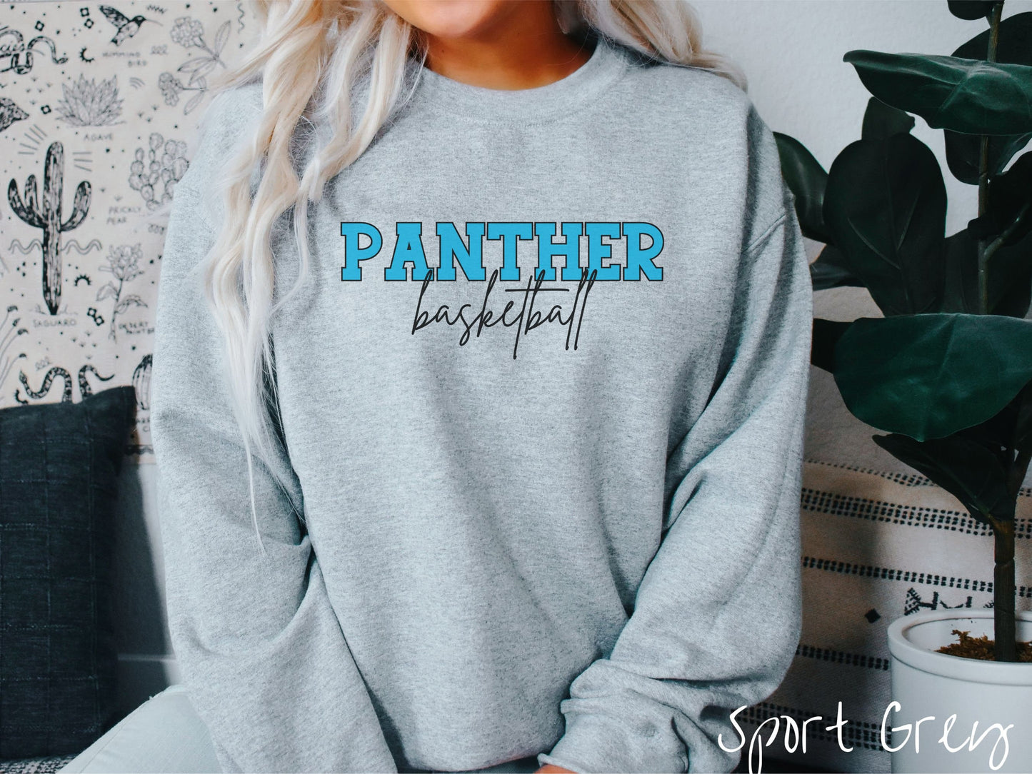 A woman wearing a cute, vintage sport grey colored sweatshirt with the word Panther in uppercase, blue font across the front and the word basketball below that in black, undercase cursive writing.