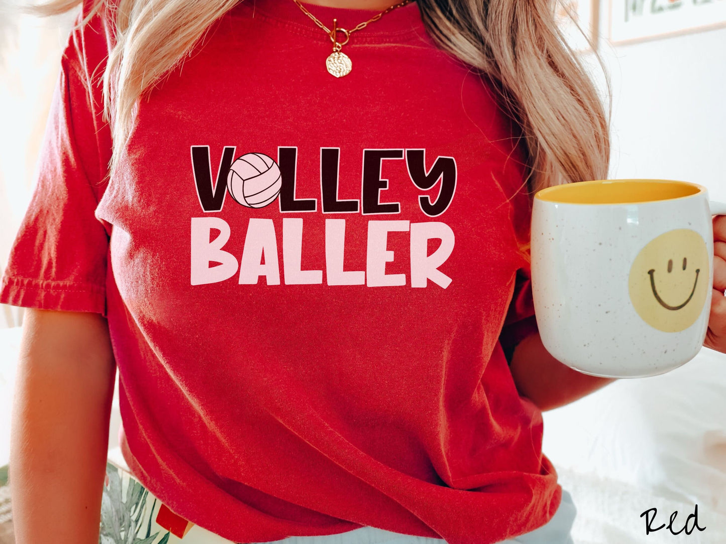A woman wearing a cute, vintage red colored Comfort Colors shirt with the word Volley across the front in black, uppercase font. The O in Volley is a white volleyball. Below that is the word Baller in white, uppercase font.