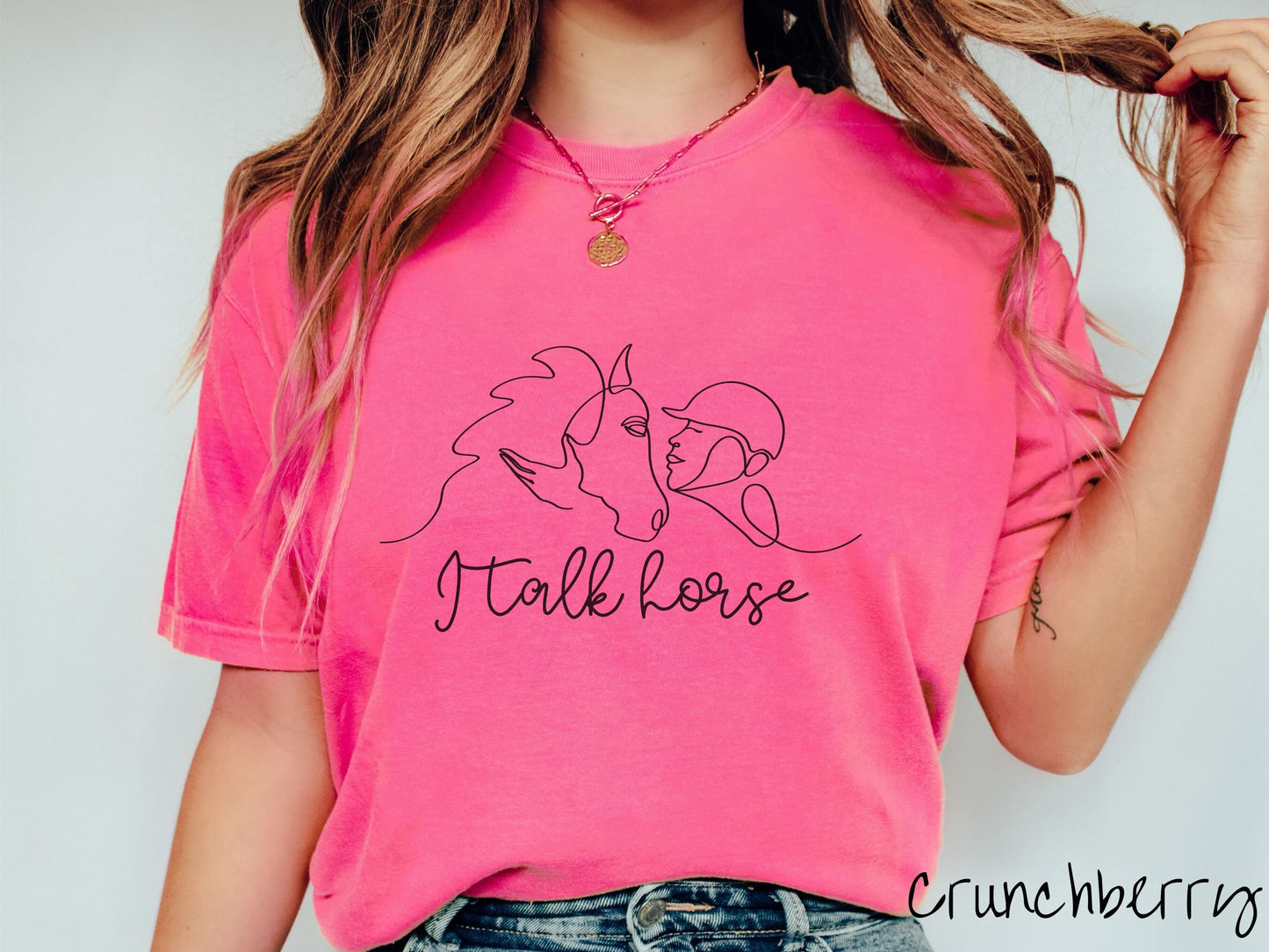 A woman wearing a cute, vintage crunchberry colored Comfort Colors shirt with a black silhouette outline of a horse jockey embracing his horse. Below that are the words I talk horse in black, cursive font.