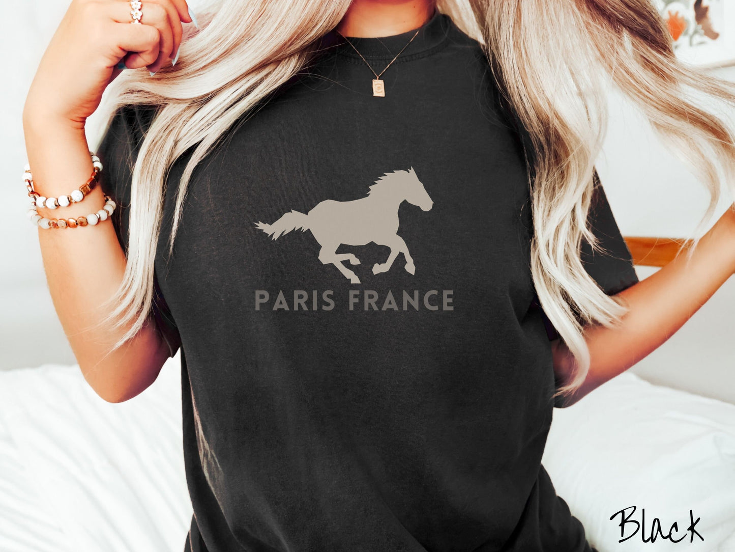 A woman wearing a cute, vintage black colored Comfort Colors shirt with a gray silhouette of a running horse across the font. Below it are the words Paris France in gray, uppercase font.