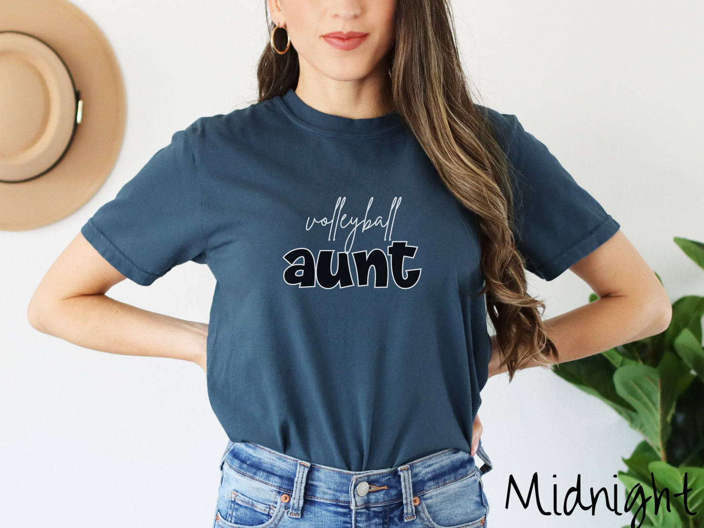 A woman wearing a cute, vintage midnight colored Comfort Colors shirt with the word volleyball across the front in white, undercase cursive writing. Below that is the word aunt in large, black font.