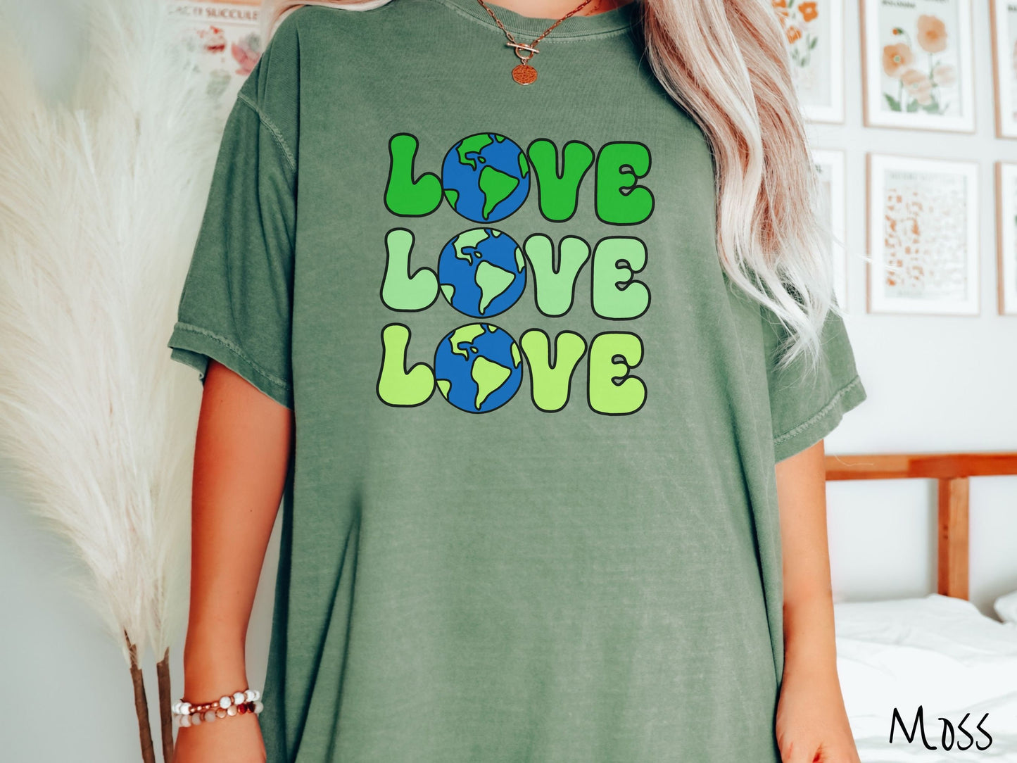 A woman wearing a cute, vintage moss colored Comfort Colors shirt with the word Love listed vertically three times in varying shades of green, uppercase font. The Os in the words are pictures of the blue and green earth.