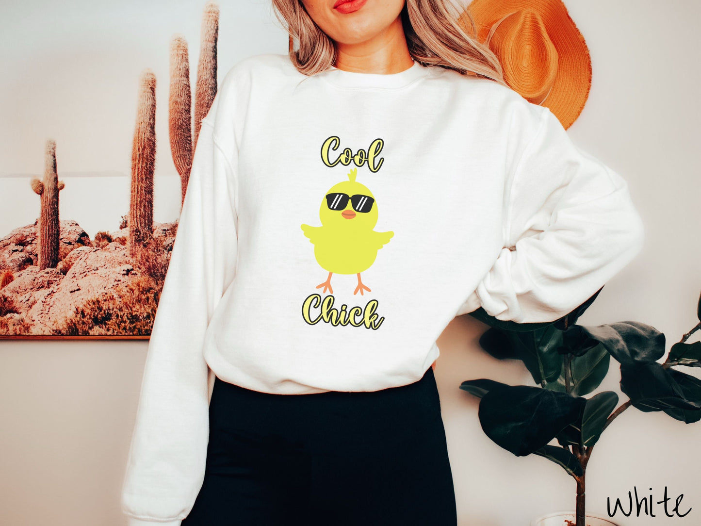 A woman wearing a cute, vintage white colored sweatshirt with yellow text Cool Chick and below is a yellow baby chick with black sunglasses with its wings spread. It has an orange mouth and feet and yellow feathers sticking out the top of its head