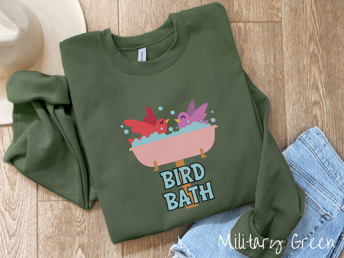 A cute, vintage military green colored comfy sweatshirt with a pink bathtub with a red bird and purple bird enjoying a bubble bath together. Below the bathtub are the words Bird Bath in light blue, uppercase font.