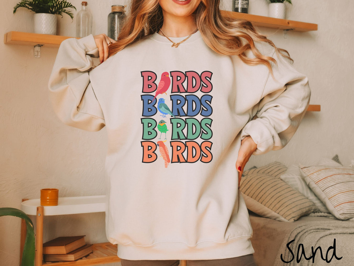 A woman wearing a cute, vintage sand colored comfy sweatshirt with the word BIRDS listed four times vertically in red, blue, green, and orange uppercase font. The Is in BIRDS are different kinds of colorful birds.