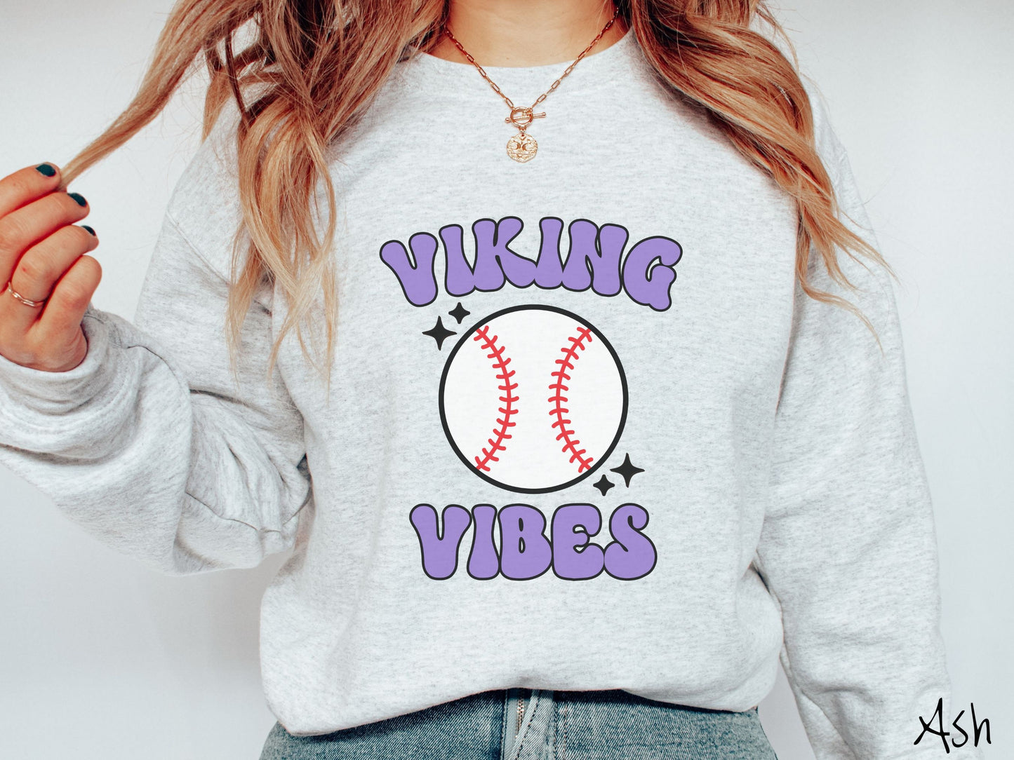 A woman wearing a cute ash colored sweatshirt with blue text saying Panther Vibes. There is a white baseball with red stitching between the text.