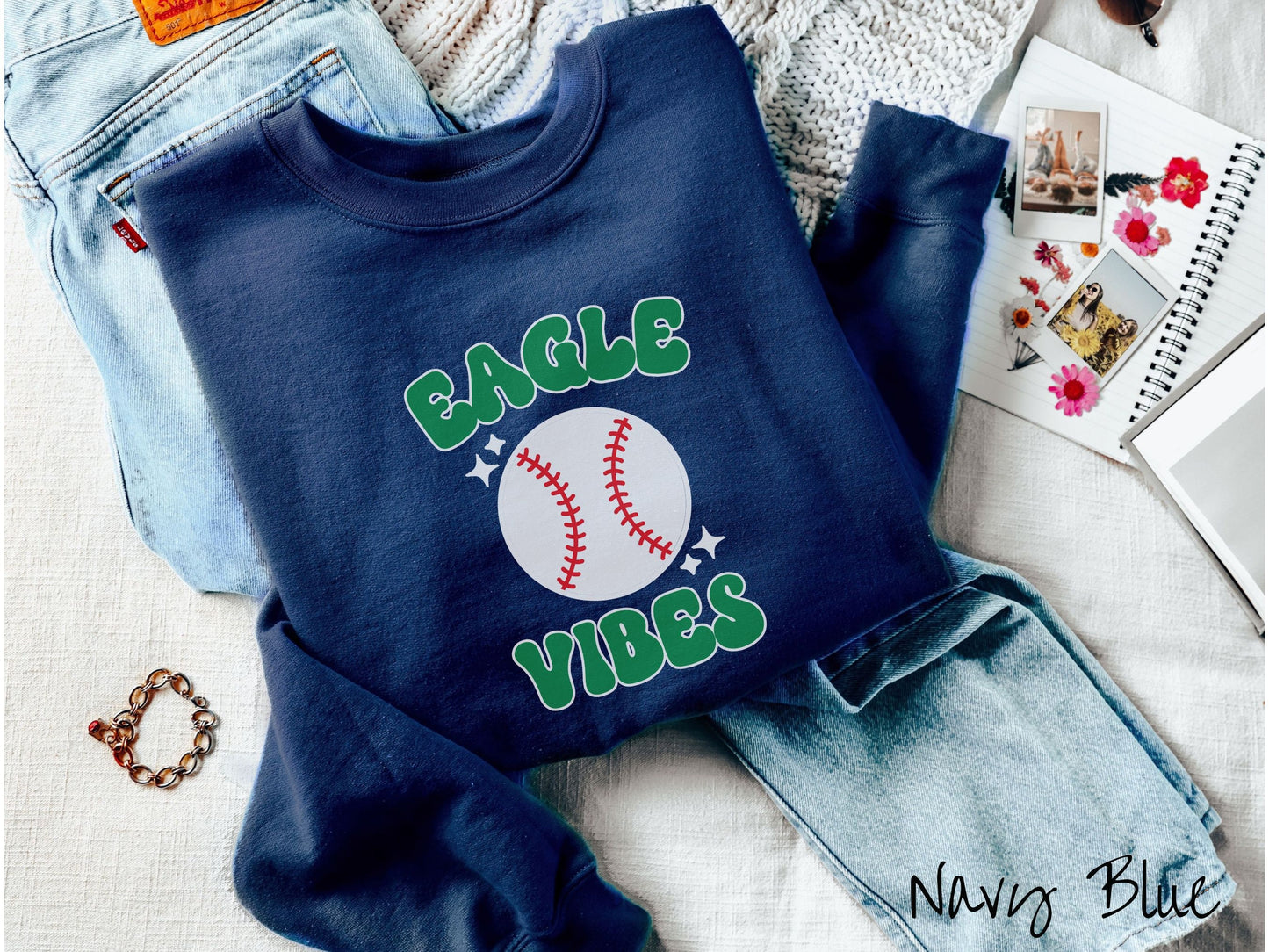A cute navy blue colored sweatshirt with green text saying Eagle Vibes. There is a white baseball with red stitching between the text.