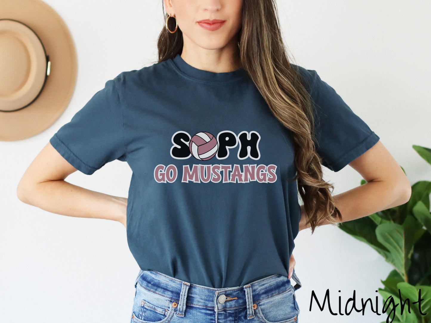 A woman wearing a cute midnight colored t-shirt with the word Soph in black and white font, the O in Soph is a purple and white volleyball. Below Soph are the words in purple and black font Go Mustangs.