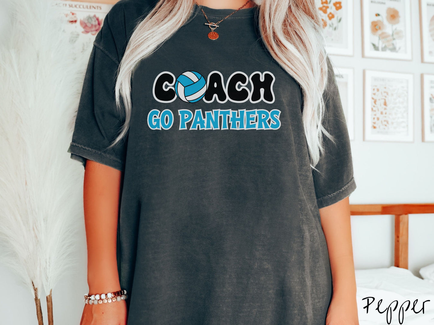 A woman wearing a cute pepper colored t-shirt with the word Coach in black and white font, the O in Coach is a blue and white volleyball. Below Coach are the words in blue and black font Go Panthers.