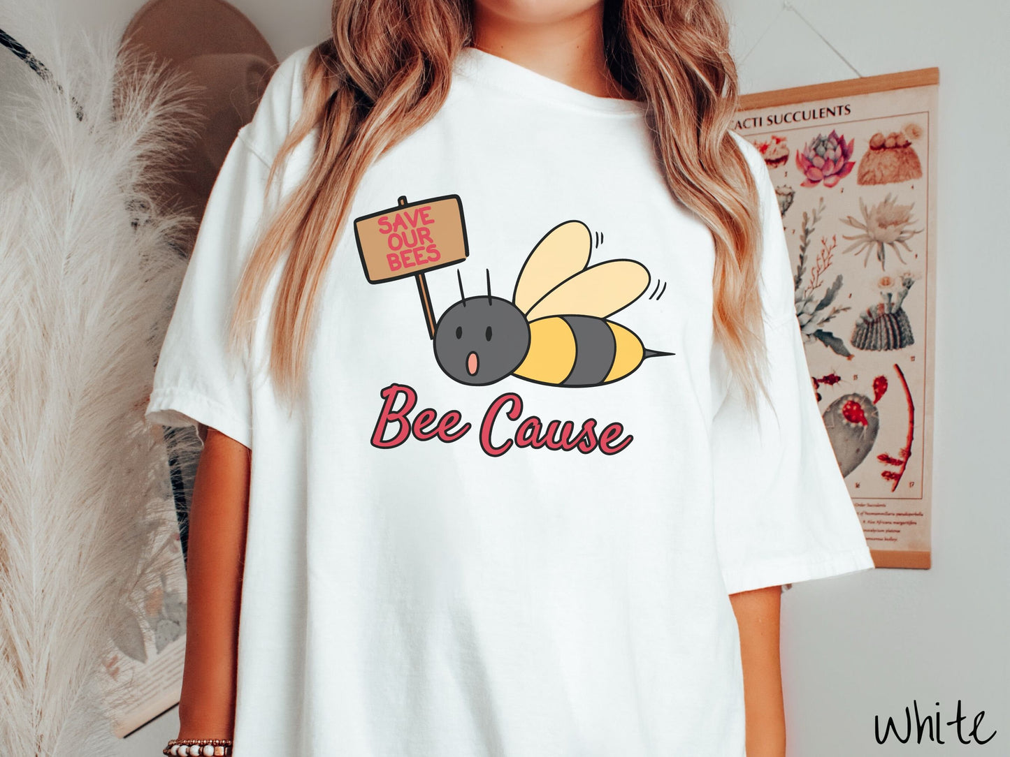 A woman wearing a cute, vintage white colored comfy sweatshirt with the text Bee Cause in red, cursive font. Above that is a black and yellow honey bee speaking with its mouth open and holding a sign that reads Save Our Bees in red font.