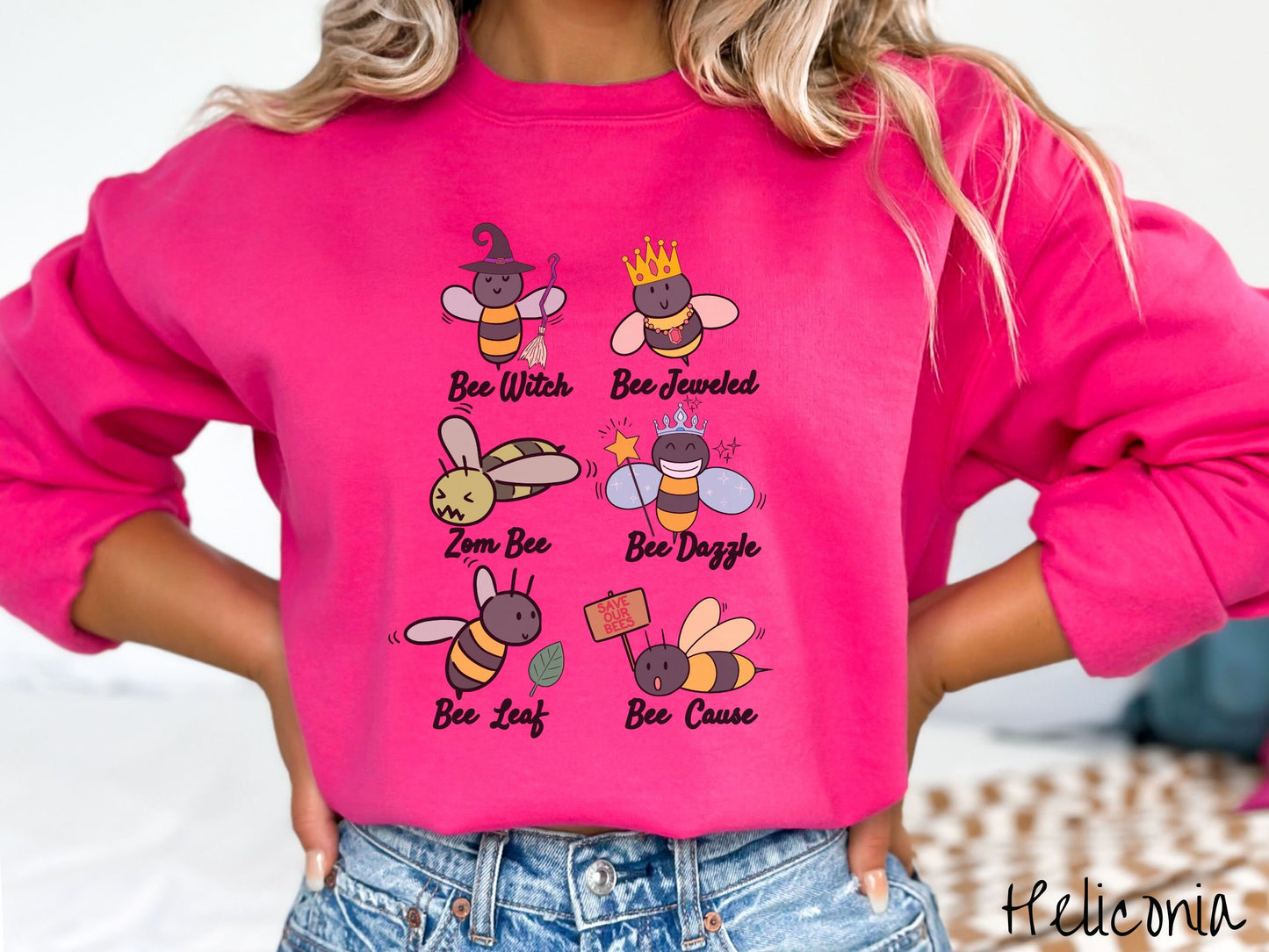 A woman wearing a cute, vintage heliconia colored comfy sweatshirt that has six puns that play on honey bees accompanied with bee drawings. The puns are Bee Witch, Bee Jeweled, Zom Bee, Bee Dazzle, Bee Leaf, and Bee Cause.