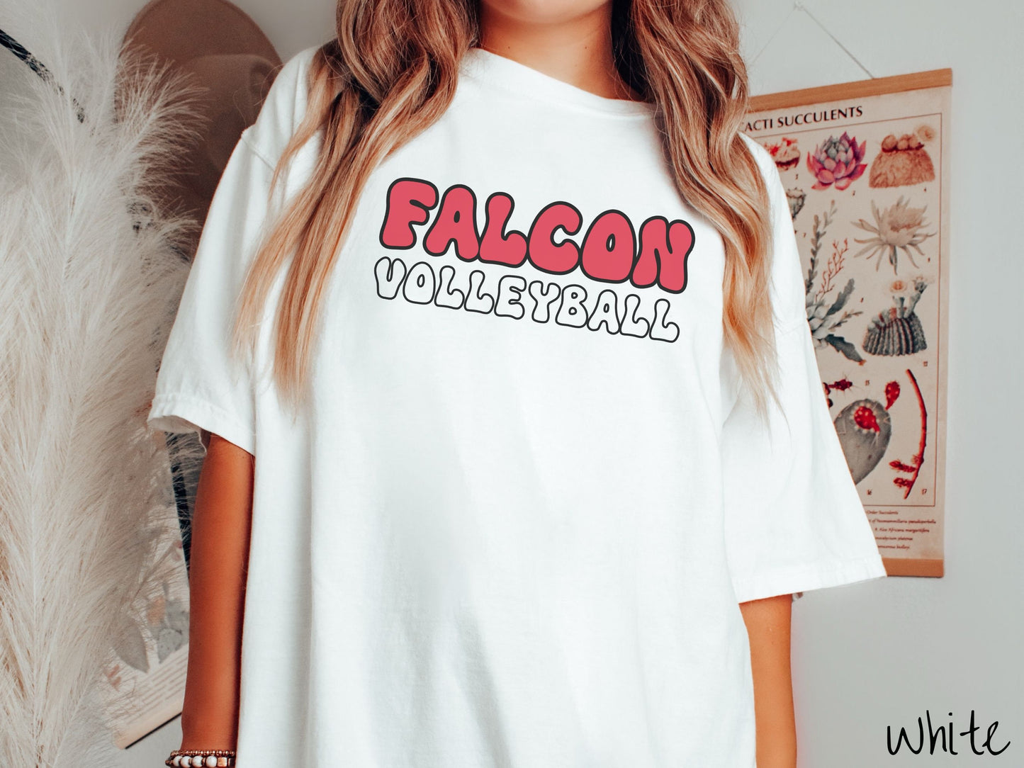 A woman wearing a cute, vintage white colored Comfort Colors shirt with the word Falcon across the front in red, uppercase font. Below that is the word Softball in white, uppercase font.