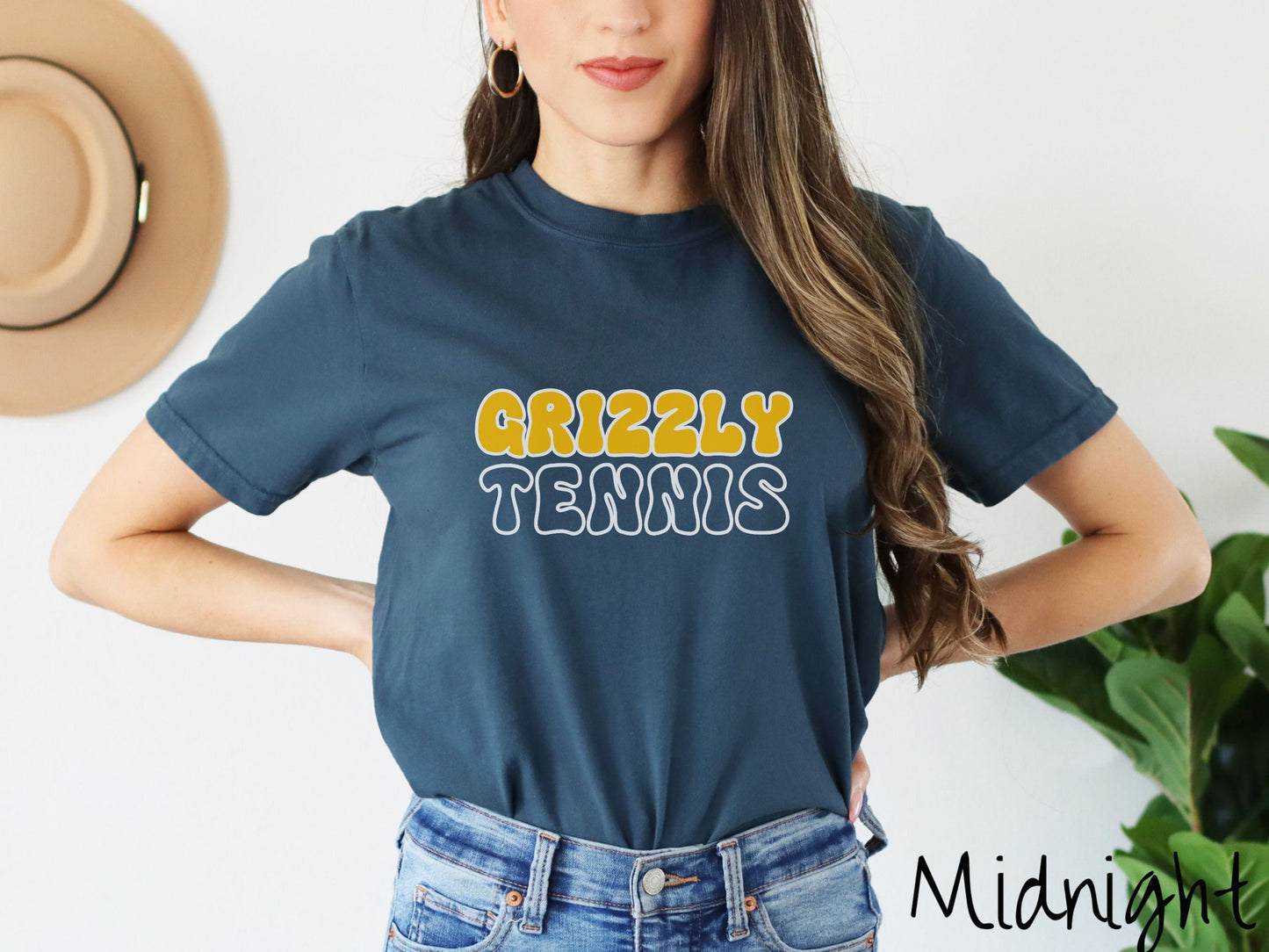 A woman wearing a cute, vintage midnight colored Comfort Colors shirt with the word Grizzly across the front in yellow, uppercase font. Below that is the word Tennis in blue, uppercase font.