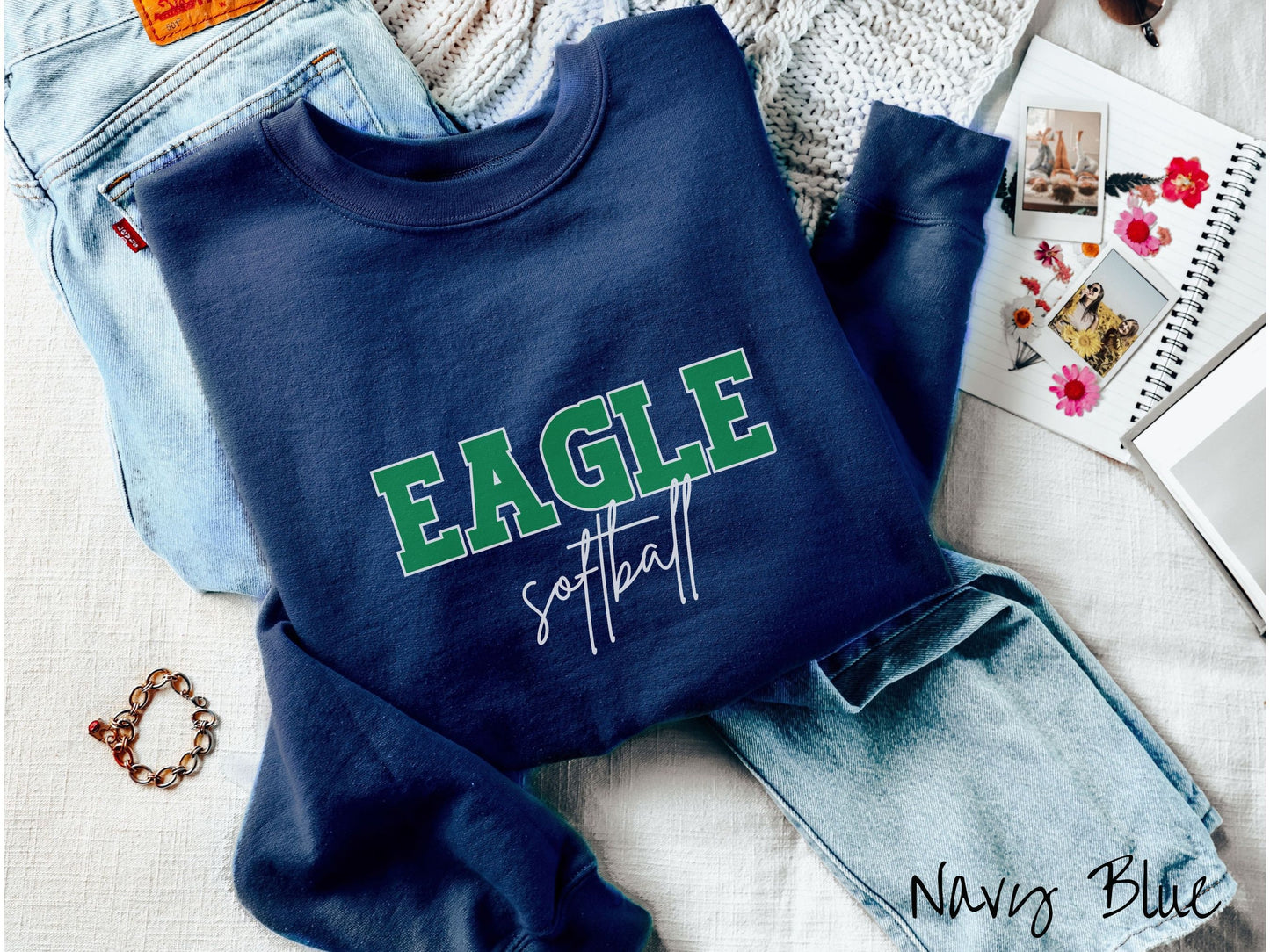 A cute, vintage navy blue colored sweatshirt with the word Eagle in uppercase, green font across the front and the word softball below that in white, undercase cursive writing.
