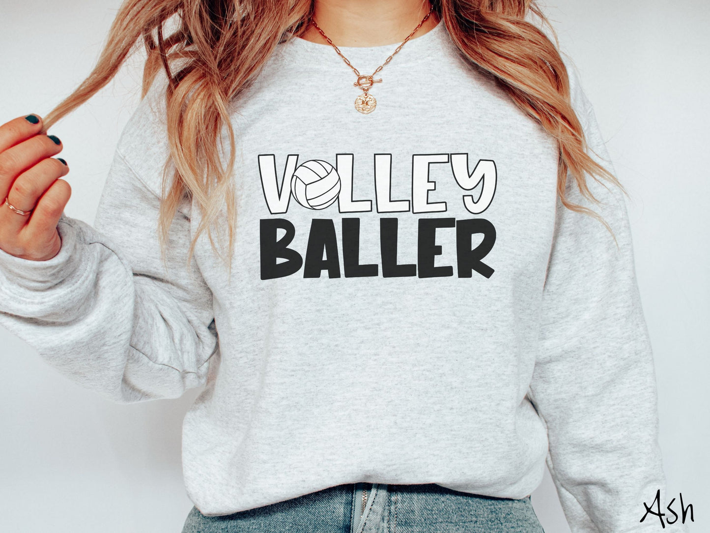 A woman wearing a cute, vintage ash colored sweatshirt with the word Volley across the front in white, uppercase font. The O in Volley is a white volleyball. Below that is the word Baller in black, uppercase font.