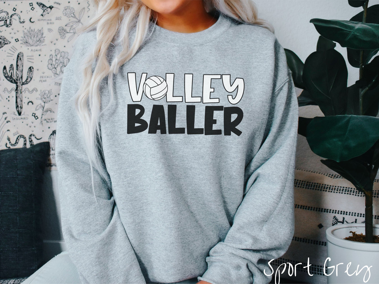 A woman wearing a cute, vintage sport grey colored sweatshirt with the word Volley across the front in white, uppercase font. The O in Volley is a white volleyball. Below that is the word Baller in black, uppercase font.