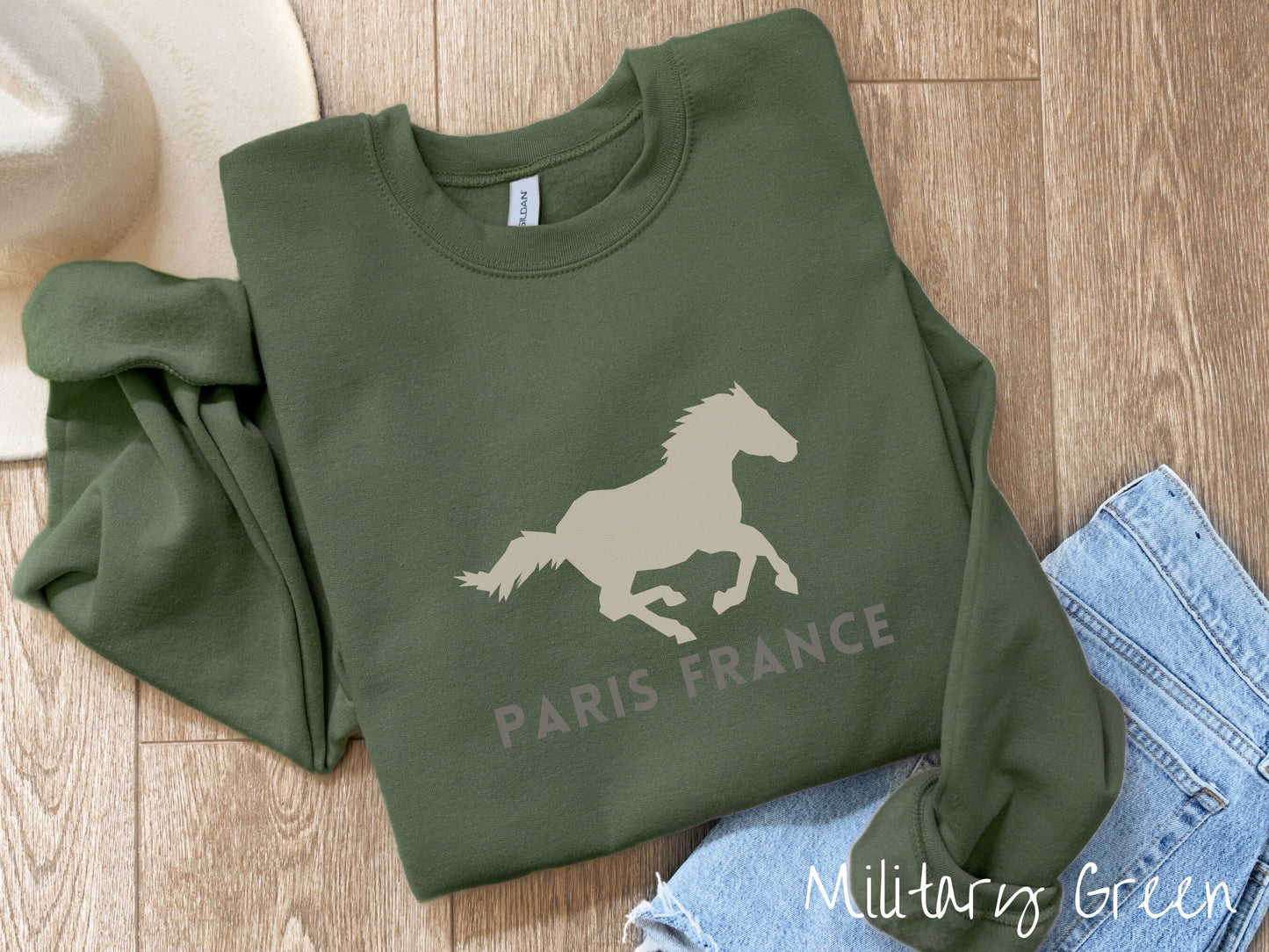 A cute, vintage military green colored comfy sweatshirt with a gray silhouette of a running horse across the font. Below it are the words Paris France in gray, uppercase font.