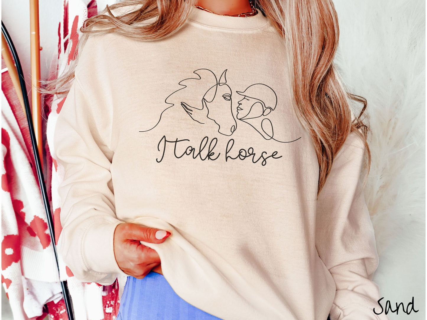 A woman wearing a cute, vintage sand colored comfy sweatshirt with a black silhouette outline of a horse jockey embracing his horse. Below that are the words I talk horse in black, cursive font.