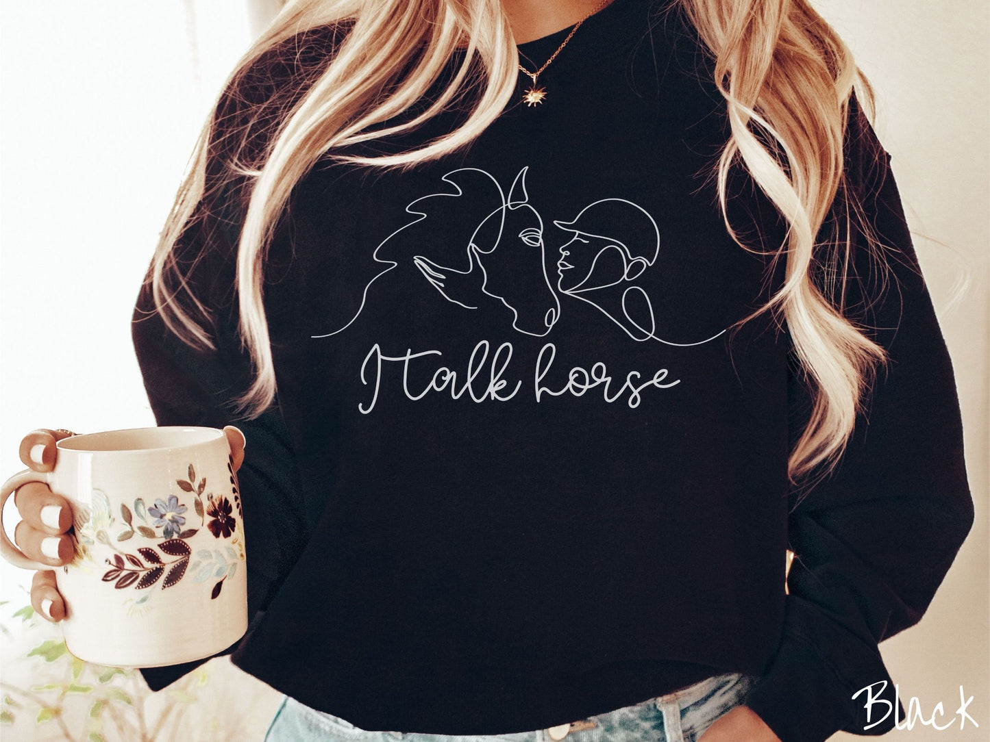 A woman wearing a cute, vintage black colored comfy sweatshirt with a white silhouette outline of a horse jockey embracing his horse. Below that are the words I talk horse in white, cursive font.
