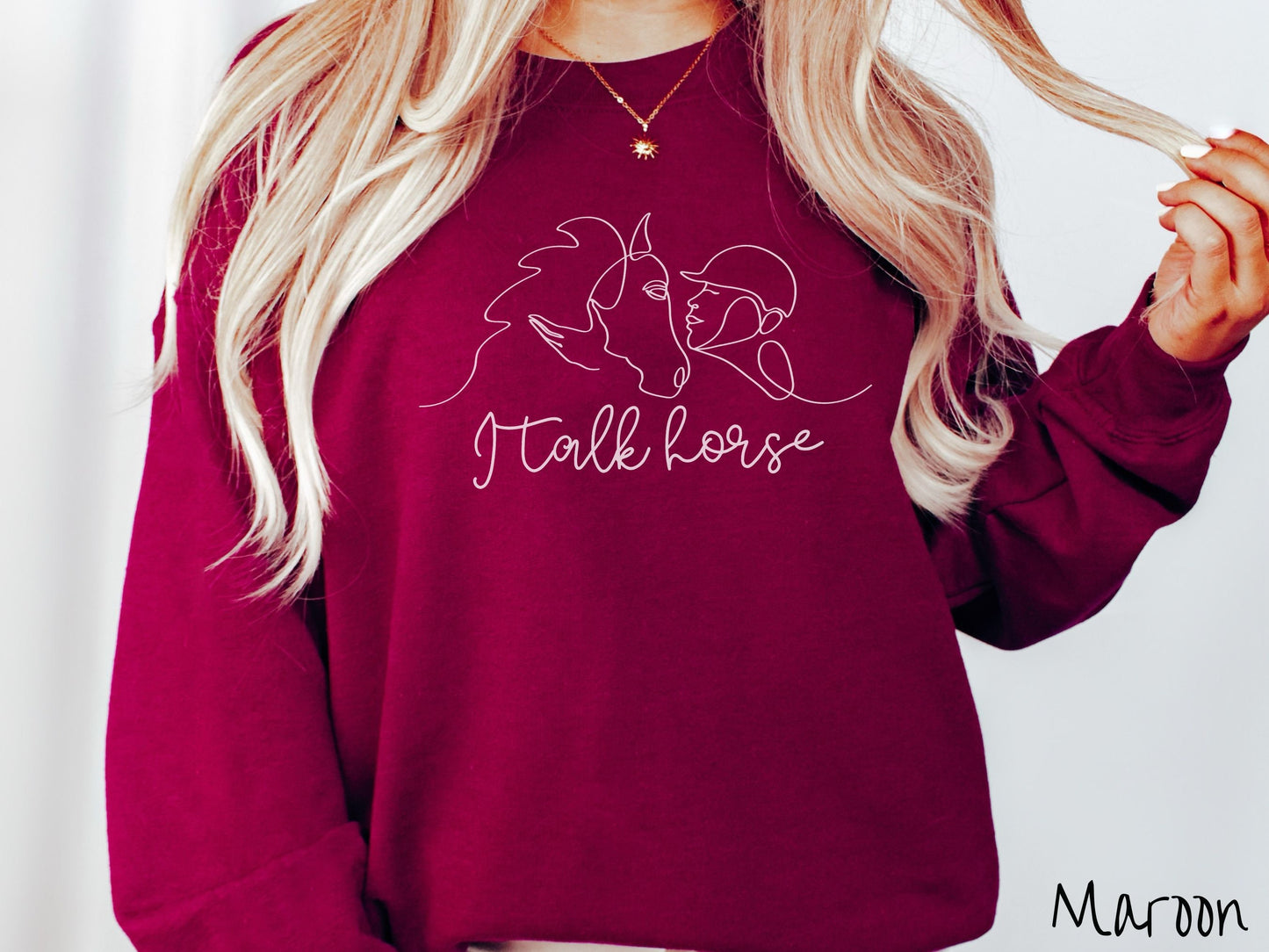 A woman wearing a cute, vintage maroon colored comfy sweatshirt with a white silhouette outline of a horse jockey embracing his horse. Below that are the words I talk horse in white, cursive font.