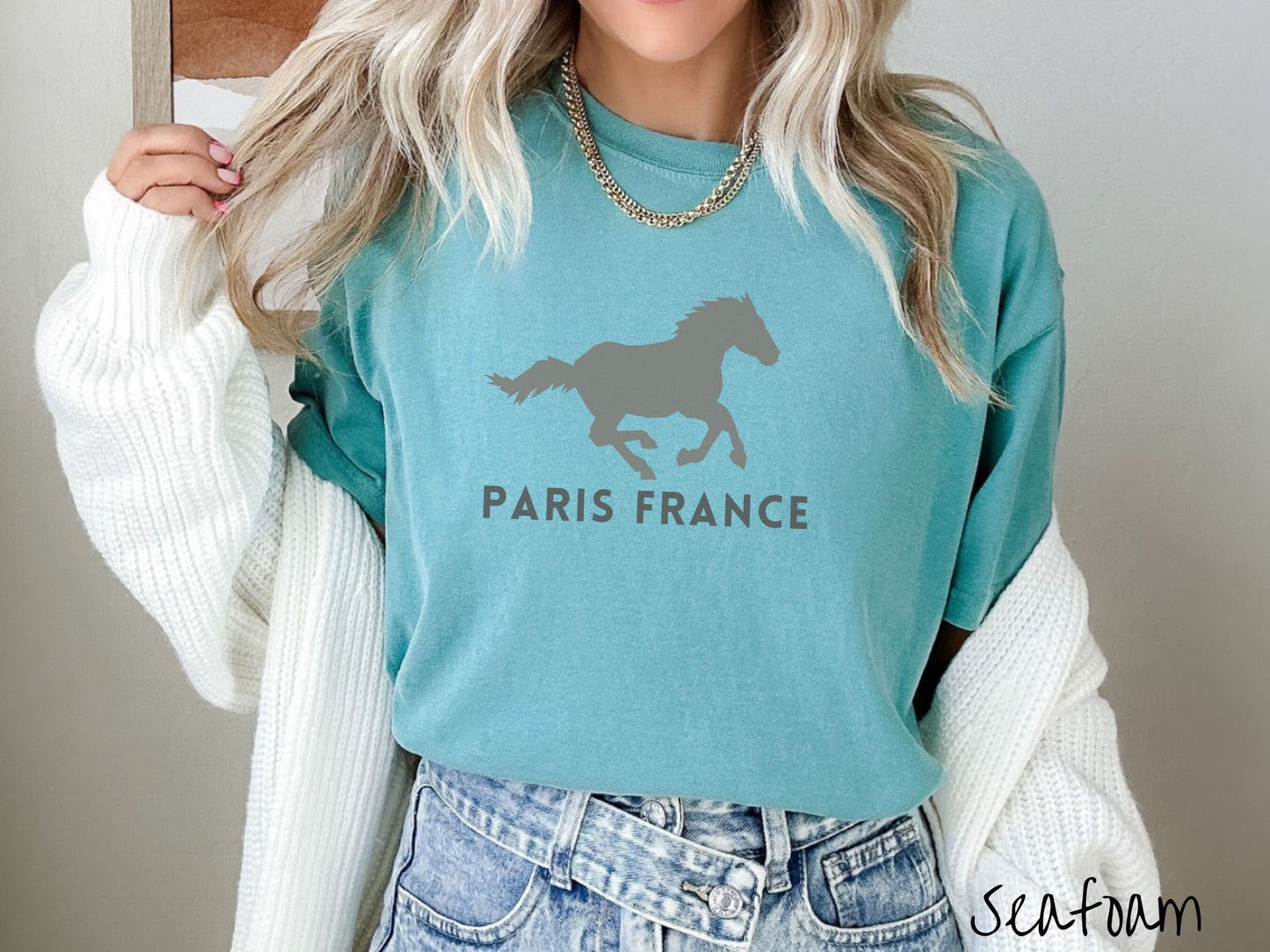 A woman wearing a cute, vintage seafoam colored Comfort Colors shirt with a gray silhouette of a running horse across the font. Below it are the words Paris France in gray, uppercase font.