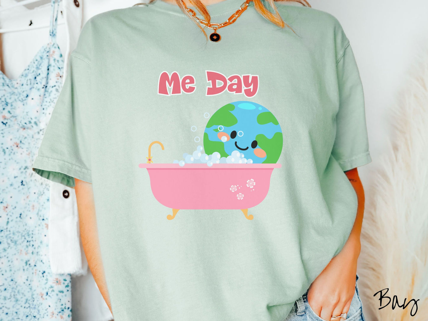 A woman wearing a cute, vintage bay colored Comfort Colors shirt with the text Me Day in red font across the top. Below that is the Earth with a smiling face sitting in a pink bathtub enjoying a bubble bath.