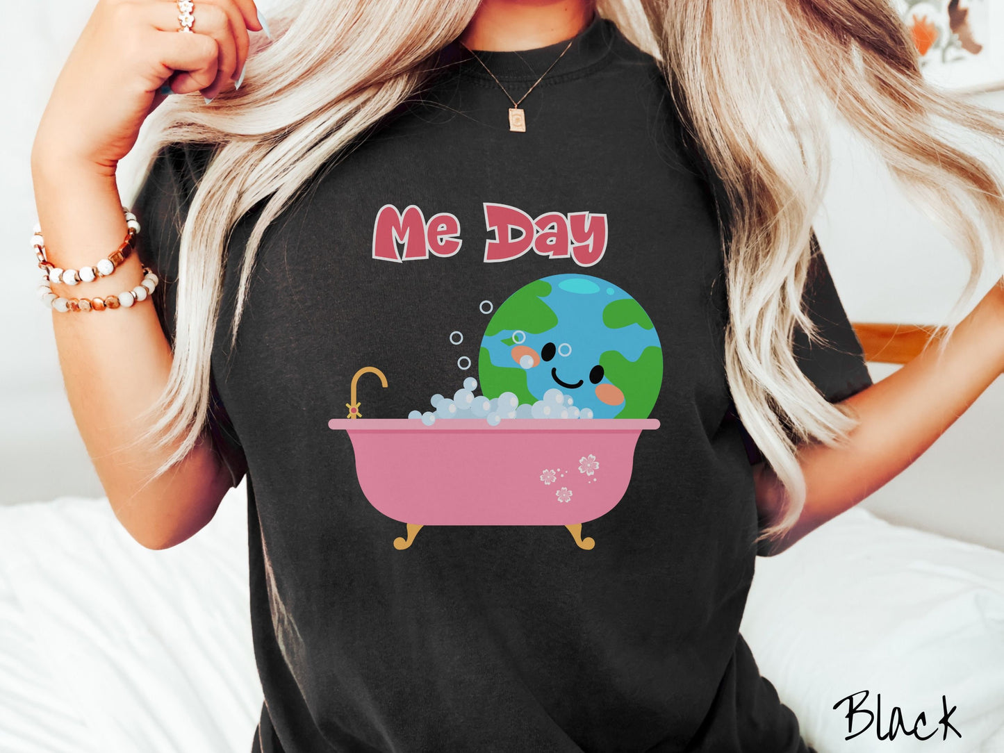 A woman wearing a cute, vintage black colored Comfort Colors shirt with the text Me Day in red font across the top. Below that is the Earth with a smiling face sitting in a pink bathtub enjoying a bubble bath.