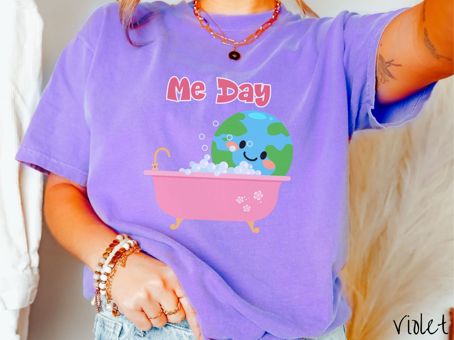 A woman wearing a cute, vintage violet colored Comfort Colors shirt with the text Me Day in red font across the top. Below that is the Earth with a smiling face sitting in a pink bathtub enjoying a bubble bath.