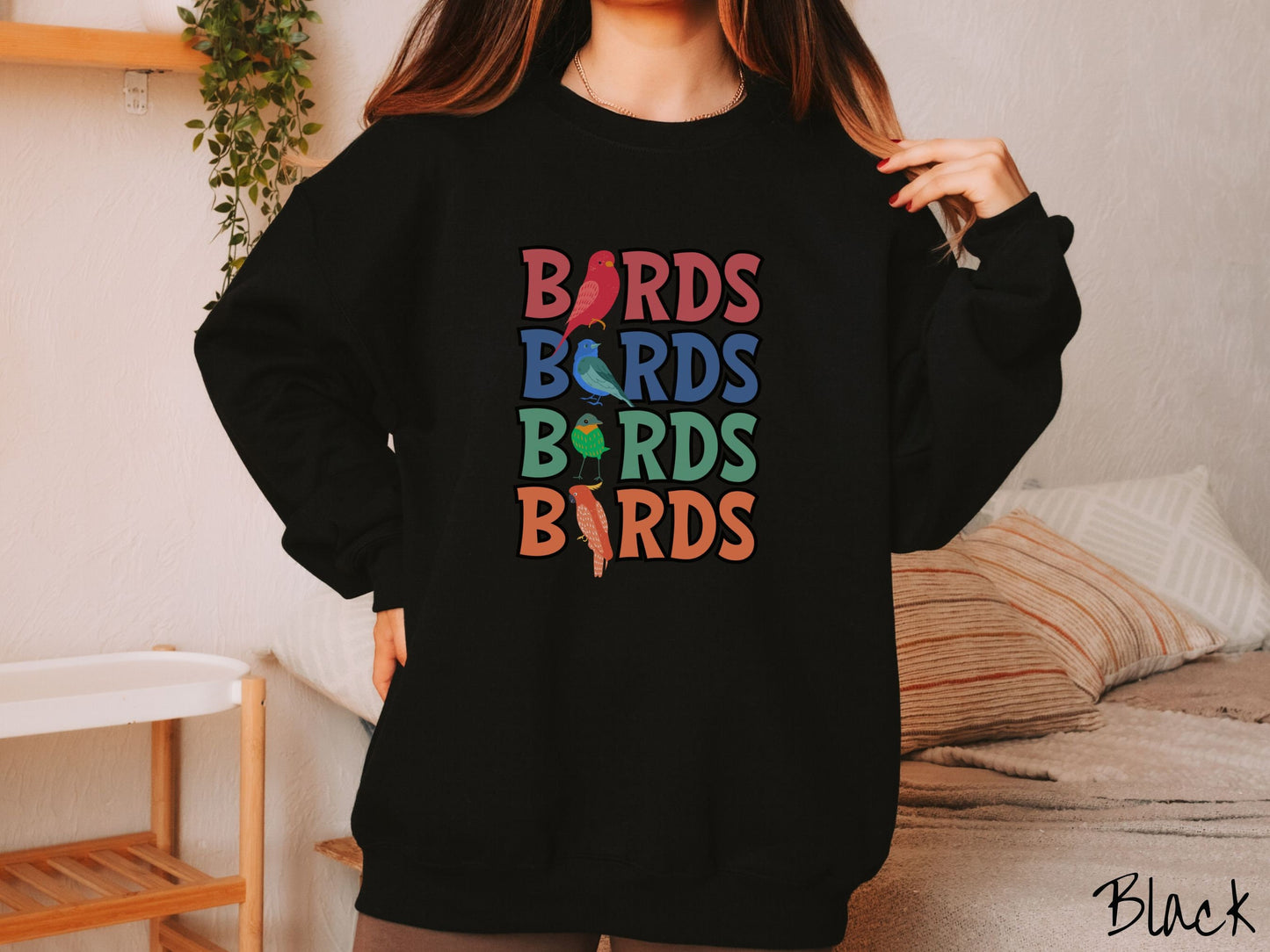 A woman wearing a cute, vintage black colored comfy sweatshirt with the word BIRDS listed four times vertically in red, blue, green, and orange uppercase font. The Is in BIRDS are different kinds of colorful birds.