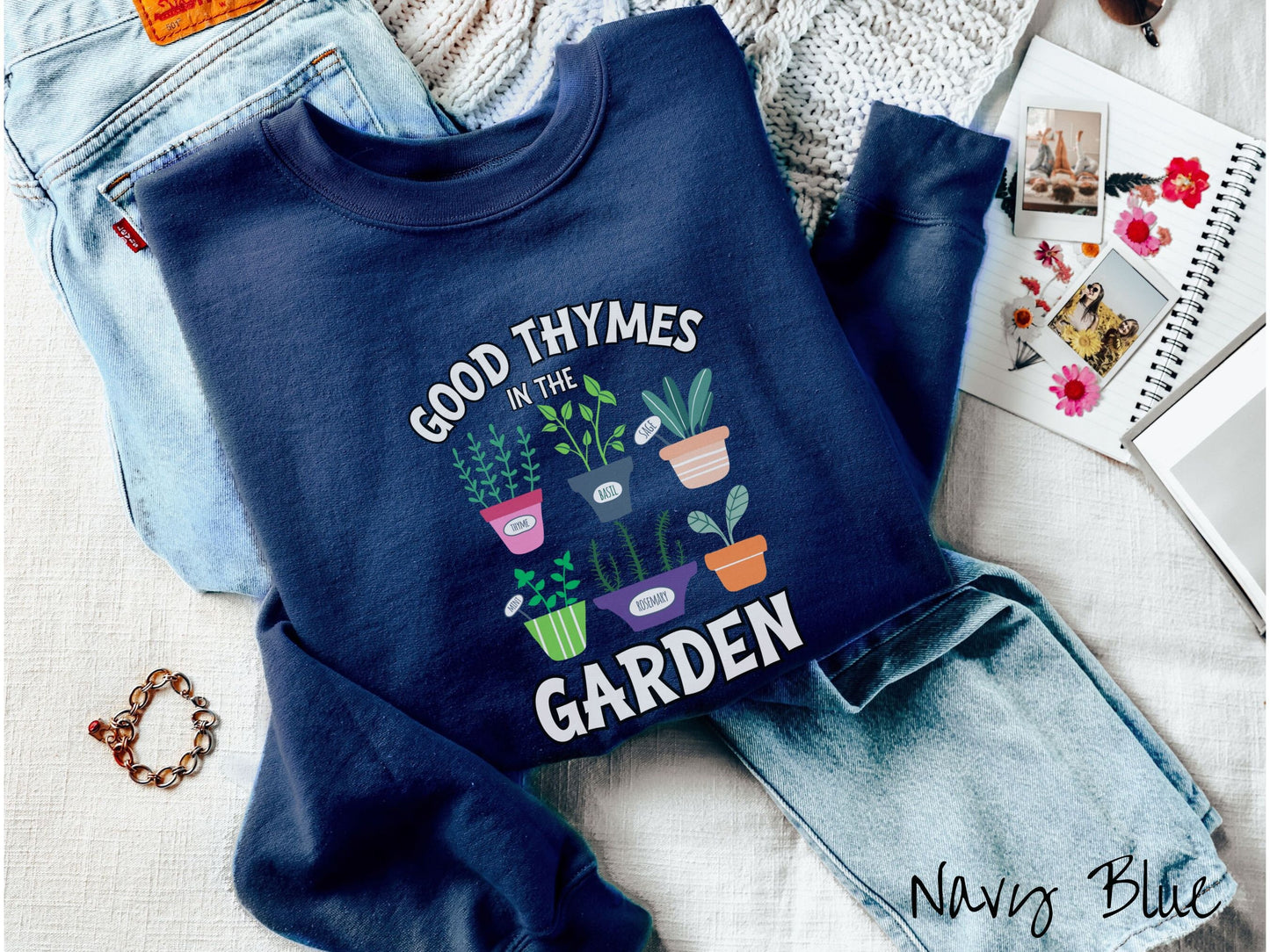 A woman wearing a cute, vintage navy blue colored comfy sweatshirt with the text Good Thymes in the Garden in white font. In between the text are different potted vegetables in colorful pots like thyme, basil, sage, and mint.