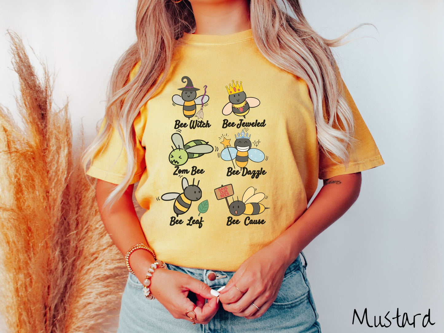 A woman wearing a cute, vintage mustard colored comfy sweatshirt that has six puns that play on honey bees accompanied with bee drawings. The puns are Bee Witch, Bee Jeweled, Zom Bee, Bee Dazzle, Bee Leaf, and Bee Cause.