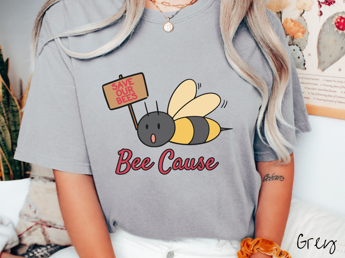 A woman wearing a cute, vintage grey colored comfy sweatshirt with the text Bee Cause in red, cursive font. Above that is a black and yellow honey bee speaking with its mouth open and holding a sign that reads Save Our Bees in red font.
