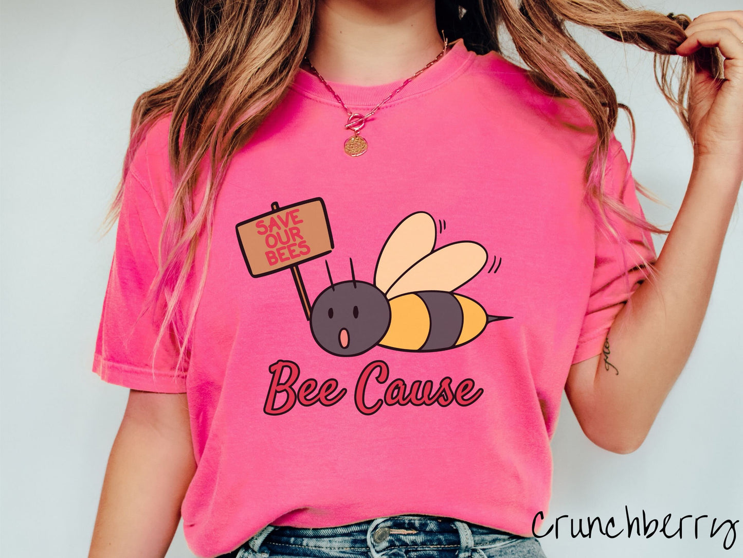 A woman wearing a cute, vintage crunchberry colored comfy sweatshirt with the text Bee Cause in red, cursive font. Above that is a black and yellow honey bee speaking with its mouth open and holding a sign that reads Save Our Bees in red font.