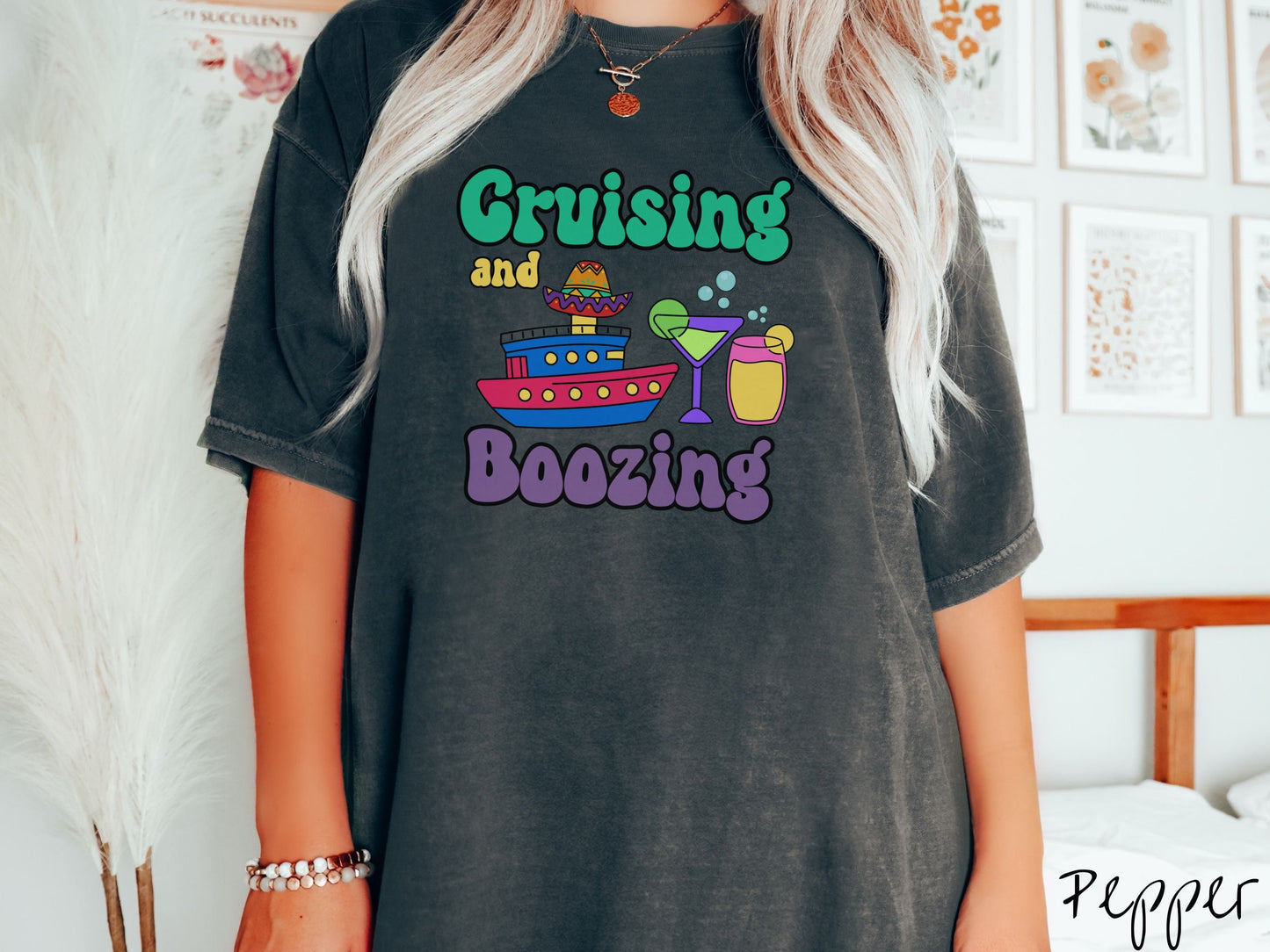 A woman wearing a cute, vintage pepper colored Comfort Colors t-shirt with text Cruising and Boozing in green, yellow, and purple font. Between the text are a colorful cruise ship wearing a sombrero and two cocktail glasses with margaritas and limes.