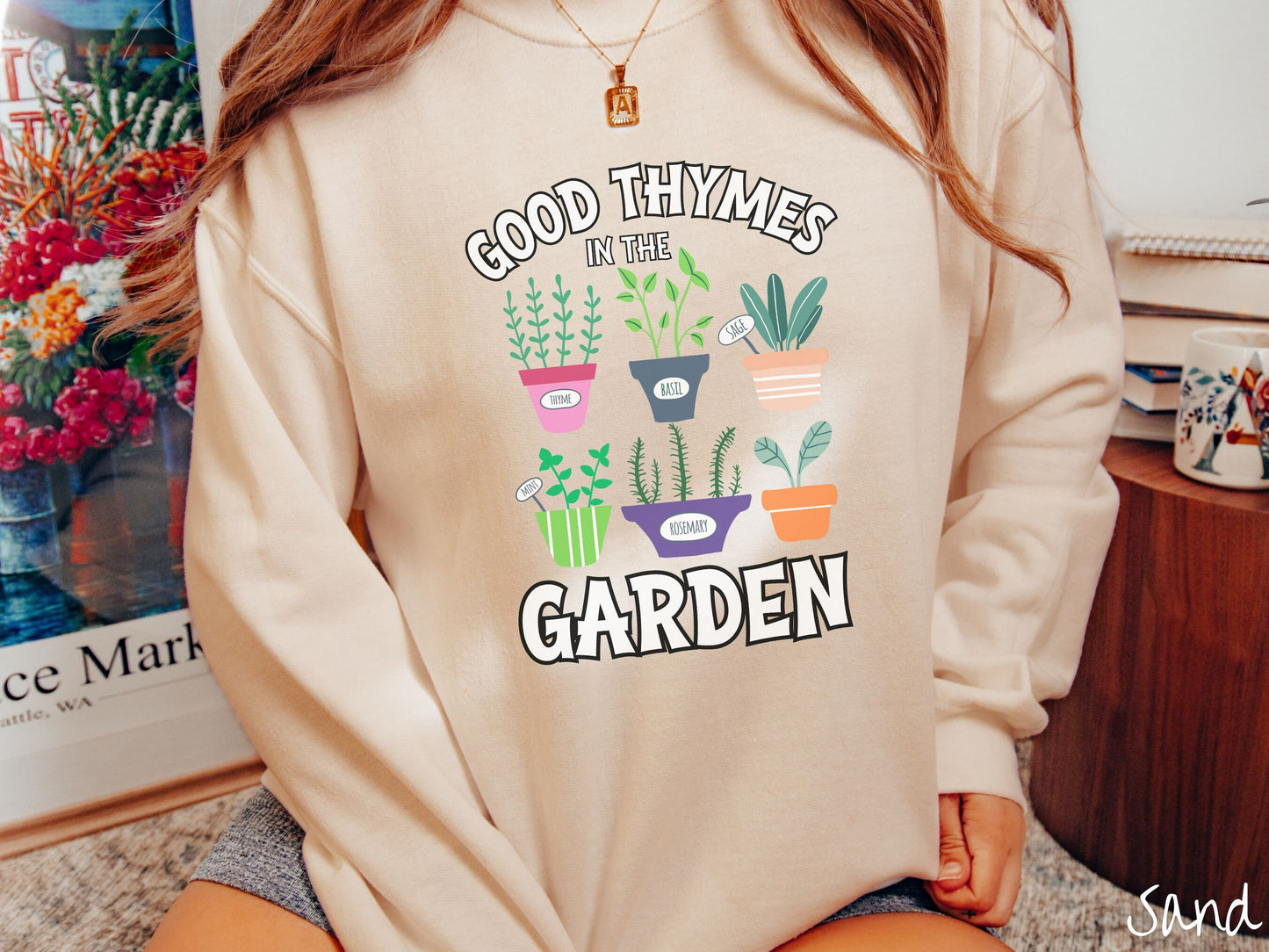 A woman wearing a cute, vintage sand colored comfy sweatshirt with the text Good Thymes in the Garden in white font. In between the text are different potted vegetables in colorful pots like thyme, basil, sage, and mint.