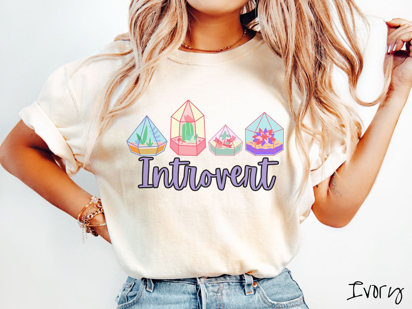 A woman wearing a cute, vintage ivory colored Comfort Colors t-shirt with the text Introvert in purple font across the front. Above the text are four colorful plant terrariums with colorful flowers and cacti inside.
