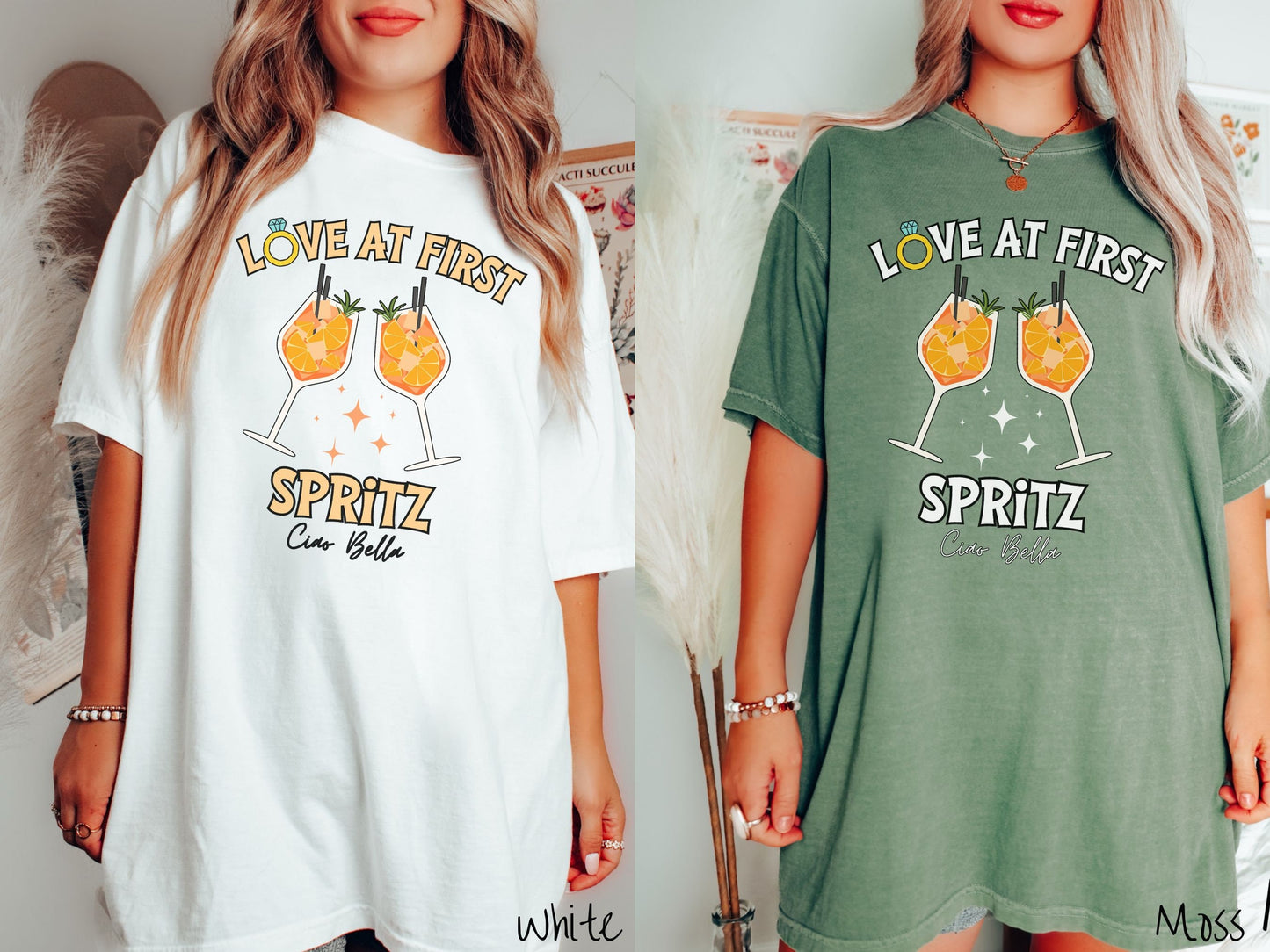 Two women wearing cute, vintage white and moss colored Comfort Colors t-shirts with text Love at First Spritz in yellow font, the O in Love is a diamond wedding ring. Between the text are two cocktail glasses of aperol spritz toasting.