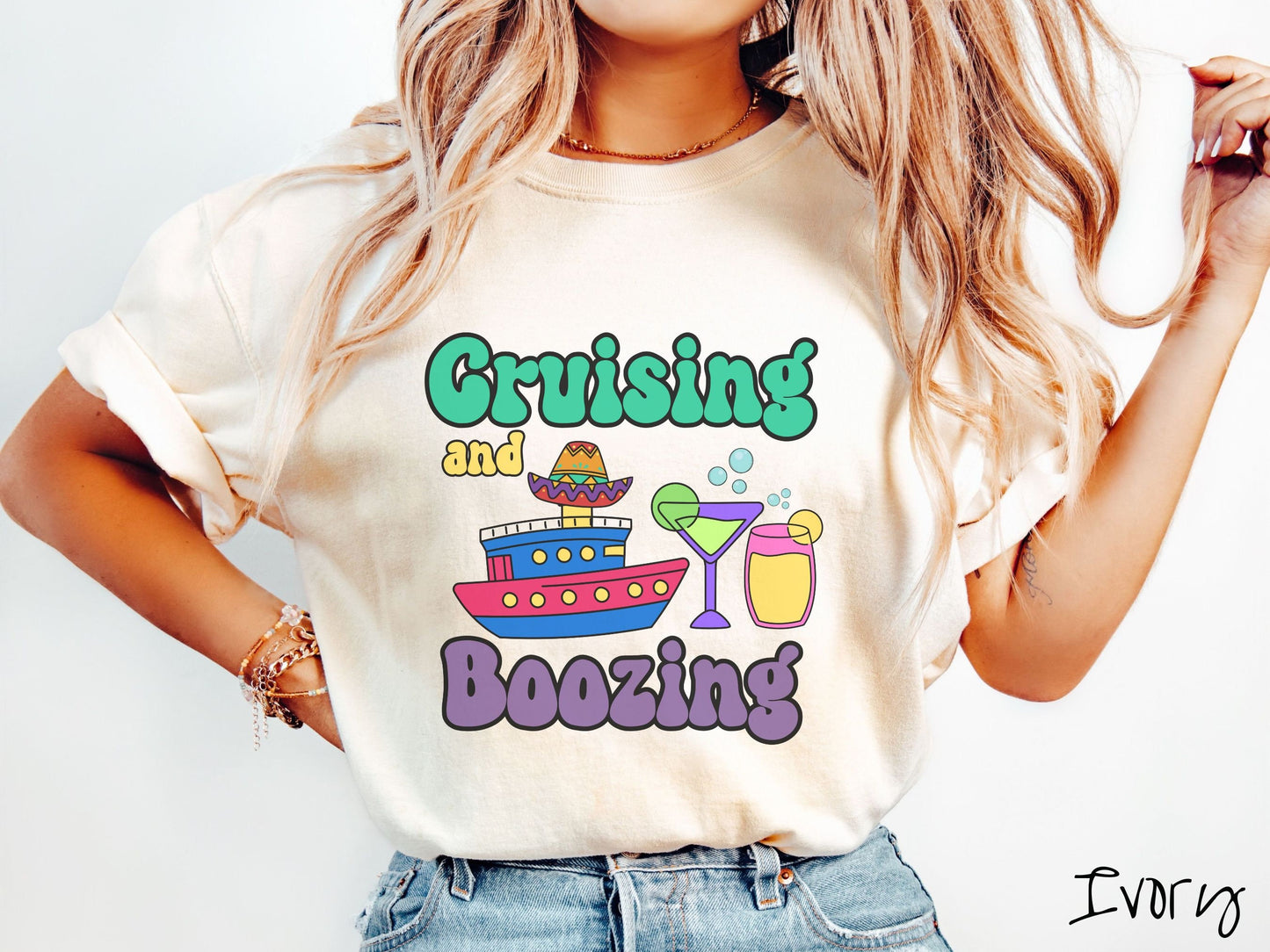 A woman wearing a cute, vintage ivory colored Comfort Colors t-shirt with text Cruising and Boozing in green, yellow, and purple font. Between the text are a colorful cruise ship wearing a sombrero and two cocktail glasses with margaritas and limes.