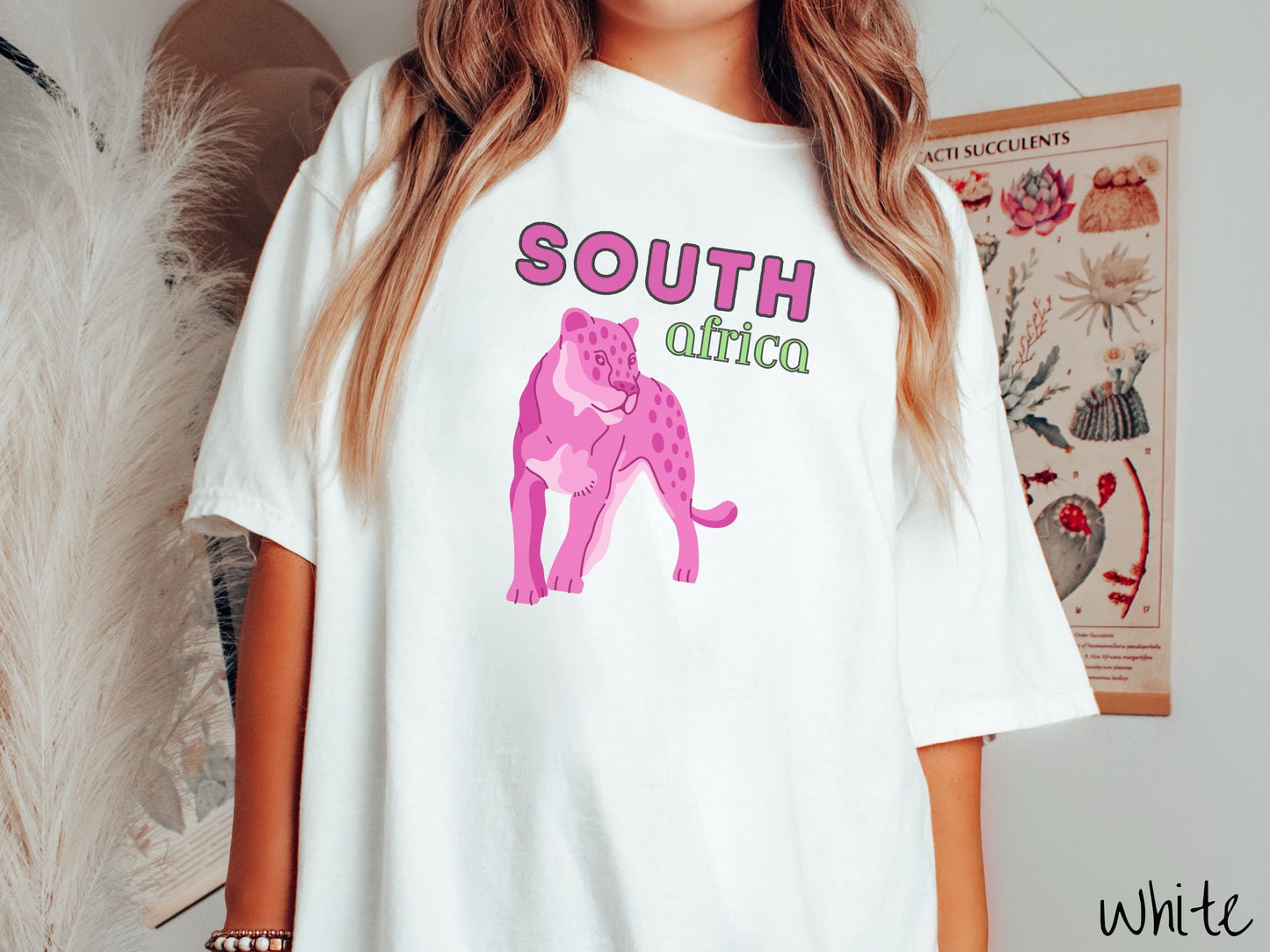 A woman wearing a vintage, white colored shirt with the text South Africa in pink and green font, respectively, and a pink tiger underneath on the prowl.