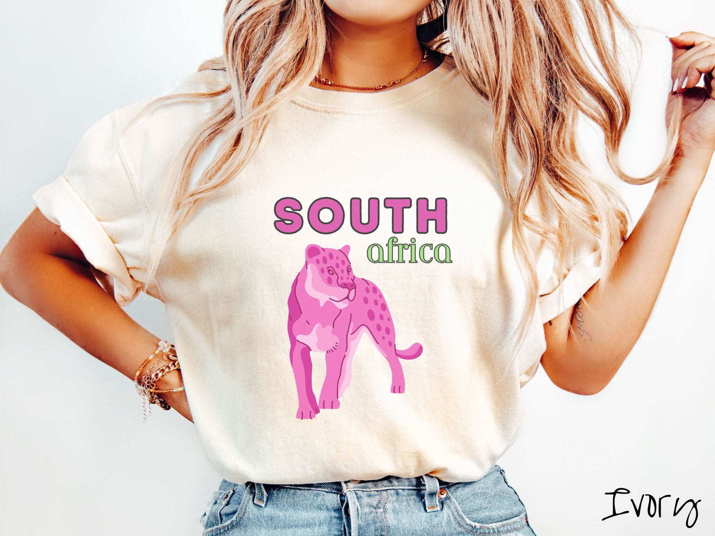 A woman wearing a vintage, ivory colored shirt with the text South Africa in pink and green font, respectively, and a pink tiger underneath on the prowl.
