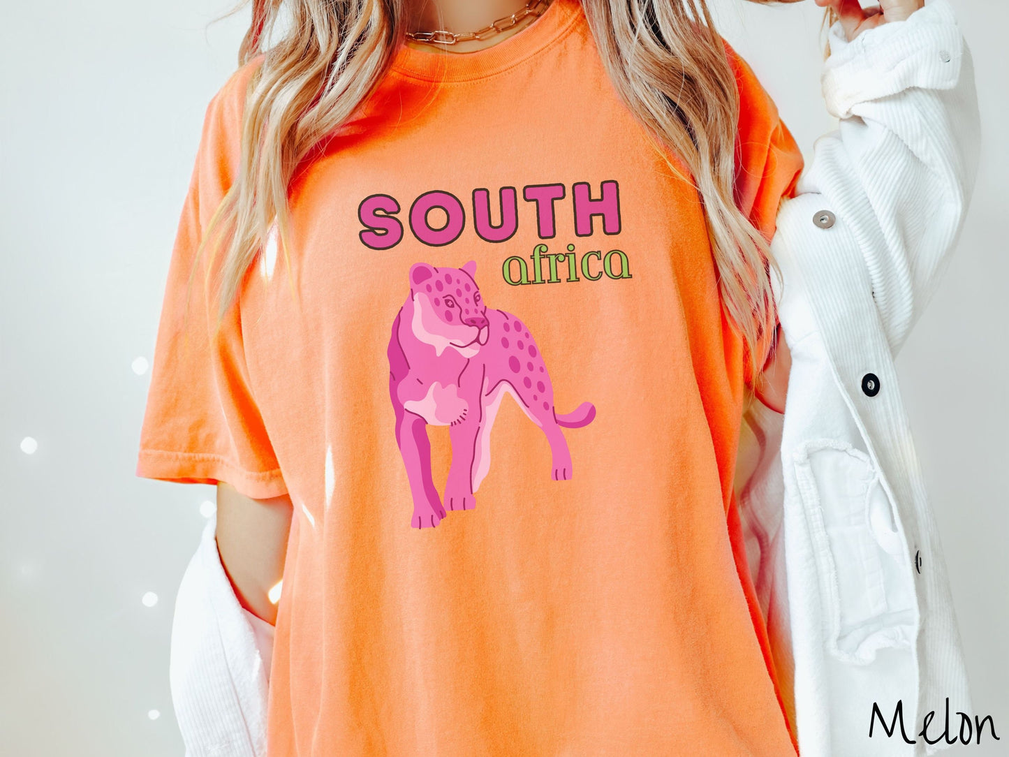 A woman wearing a vintage, melon colored shirt with the text South Africa in pink and green font, respectively, and a pink tiger underneath on the prowl.